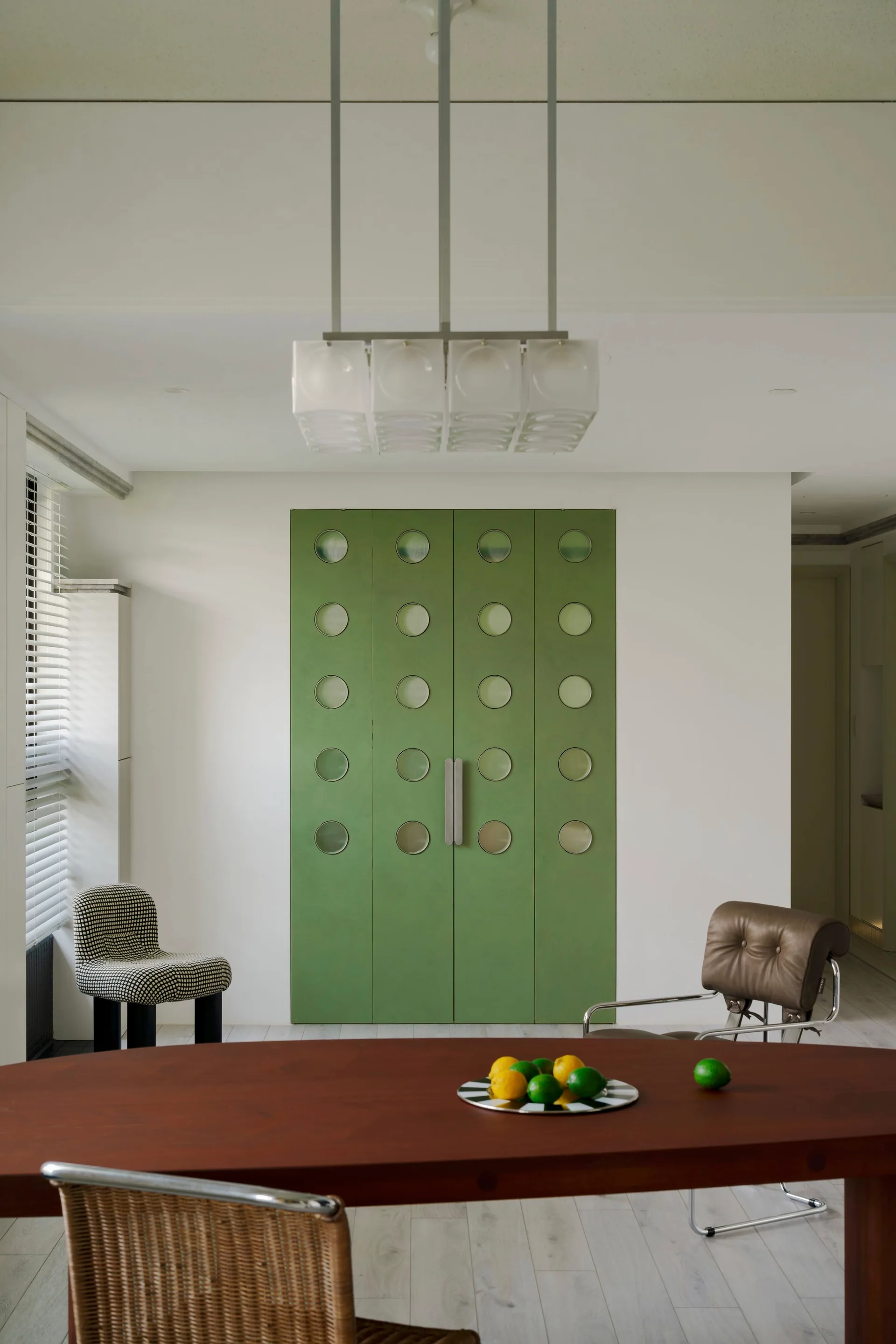 A dining room features an oval wood table in the foreground and a set of bright green double doors with circular glass panels in the background.