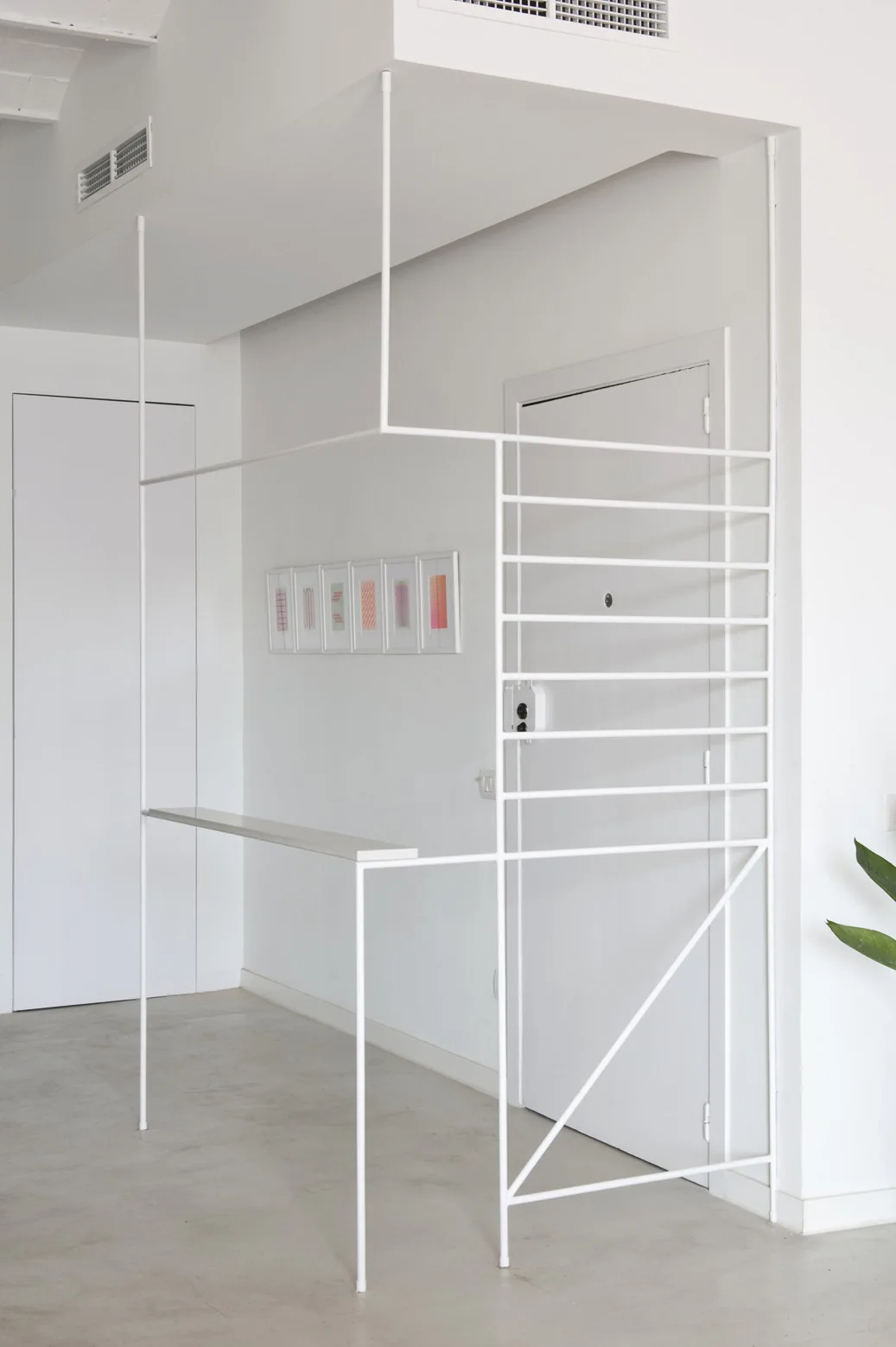 A minimalist white metal rod partition with an integrated shelf stands in a modern white entryway with a light gray floor.