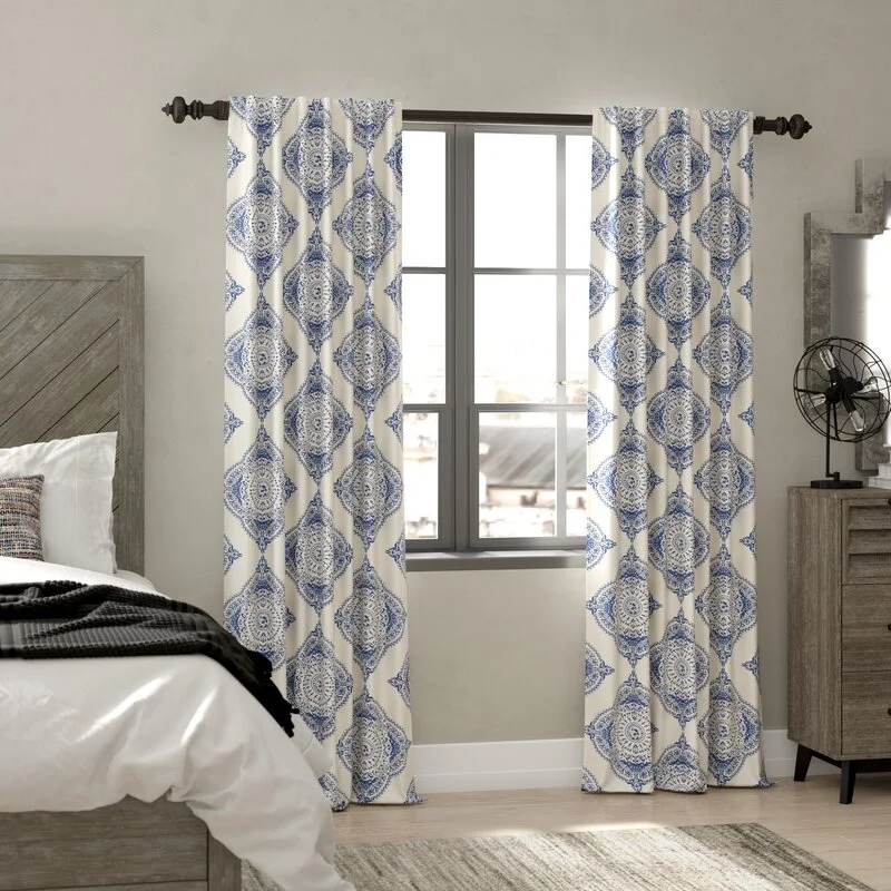 Blue and white patterned curtains hang beside a bedroom window next to a rustic wooden headboard and a tall wood-grained dresser.