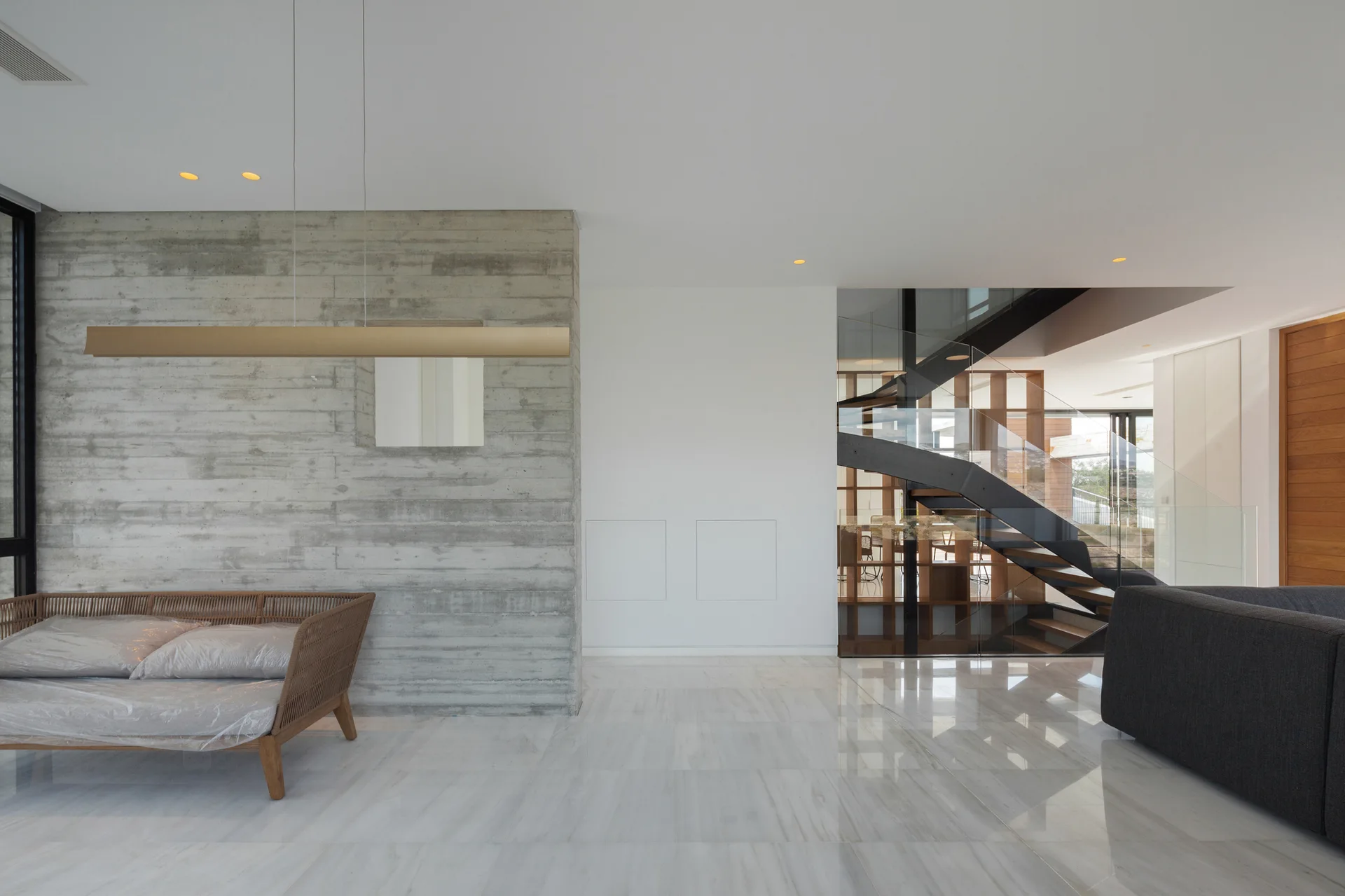 A modern open-plan living room with a textured concrete accent wall, a floating metal staircase, and polished white marble tile flooring.