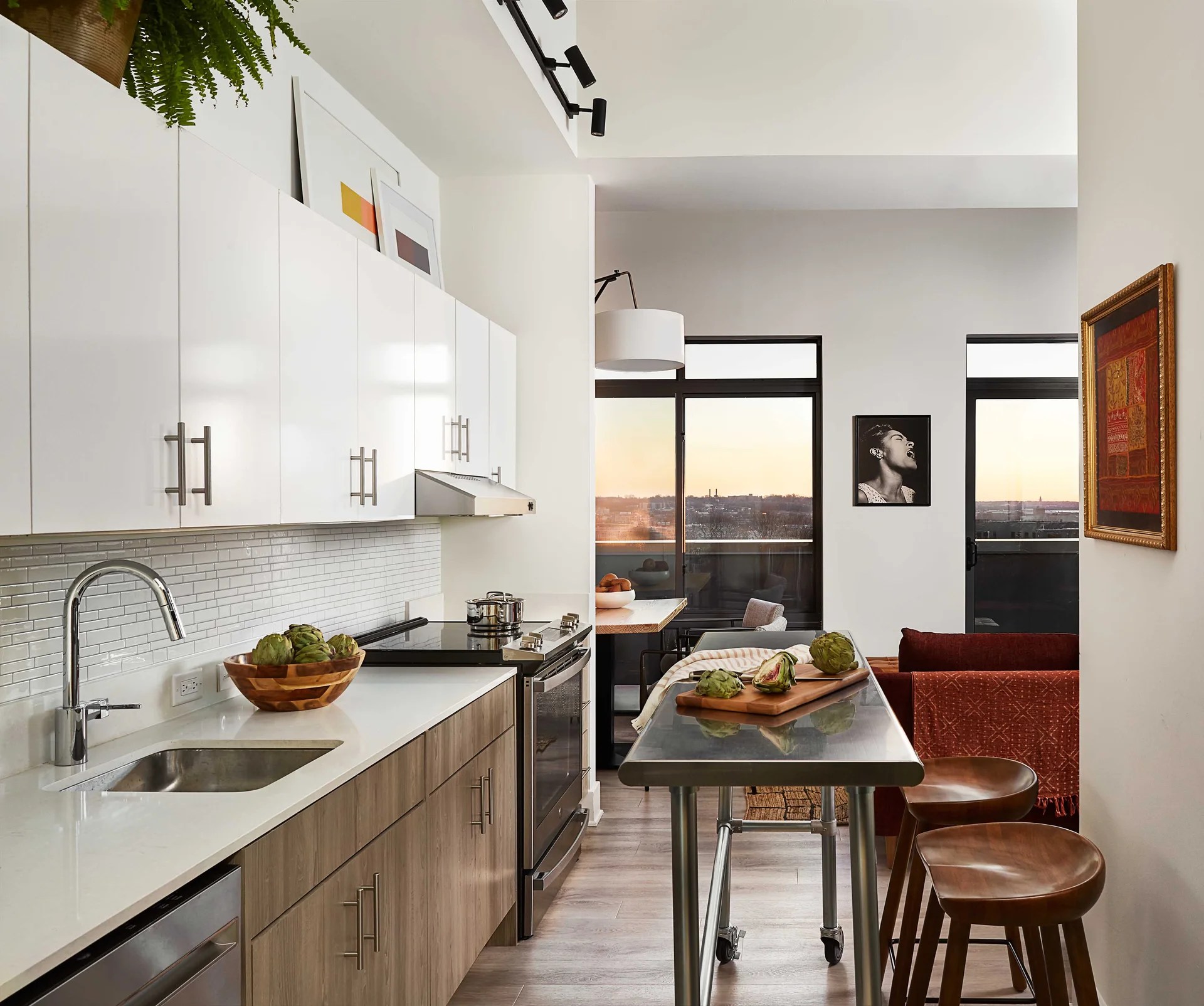 A modern kitchen featuring glossy white upper cabinets, wood-grained lower cabinets, and a metal prep island with two curved wooden stools.