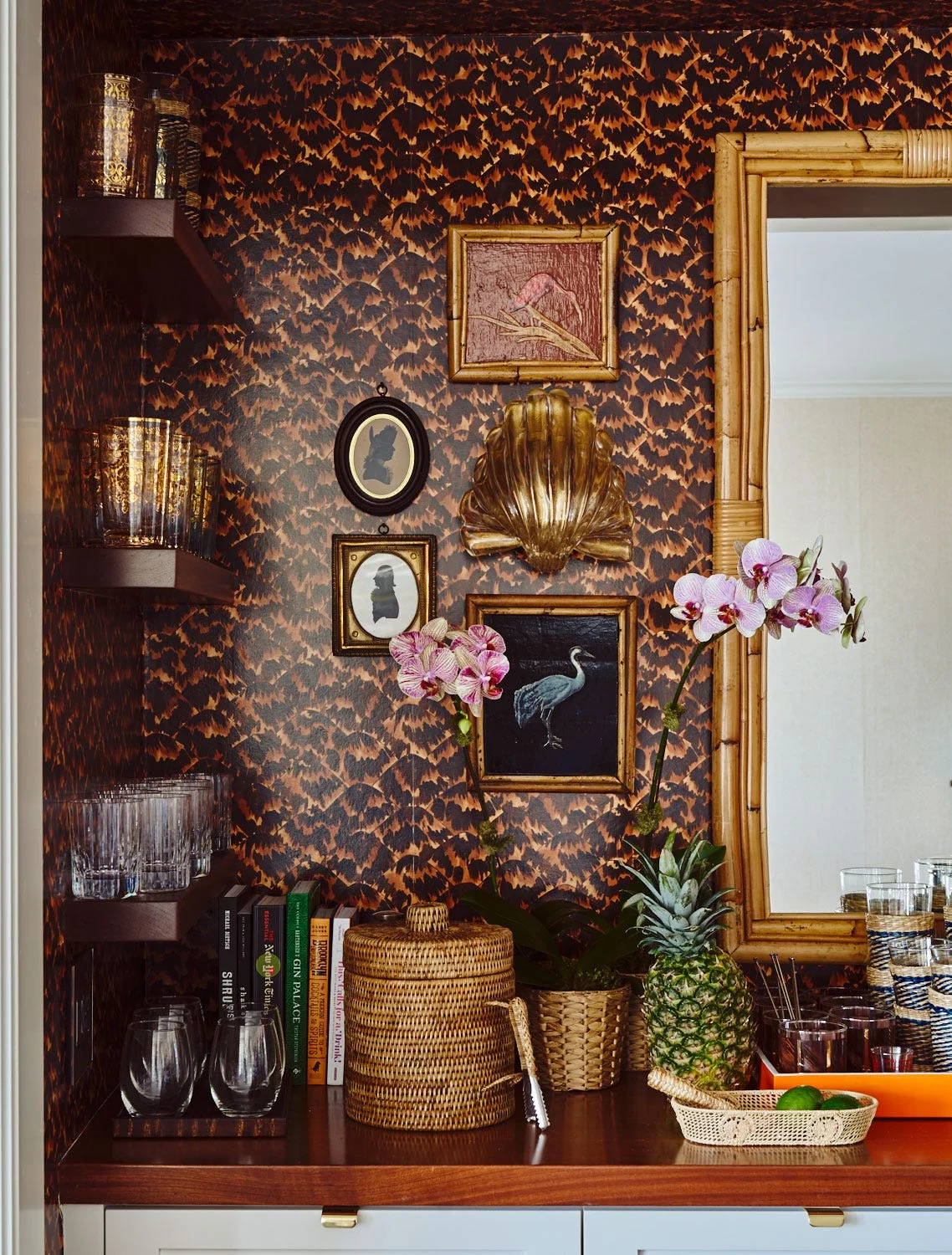 A home bar area features dark tortoiseshell wallpaper, floating wooden shelves with glassware, small framed art, and a bamboo-framed mirror.