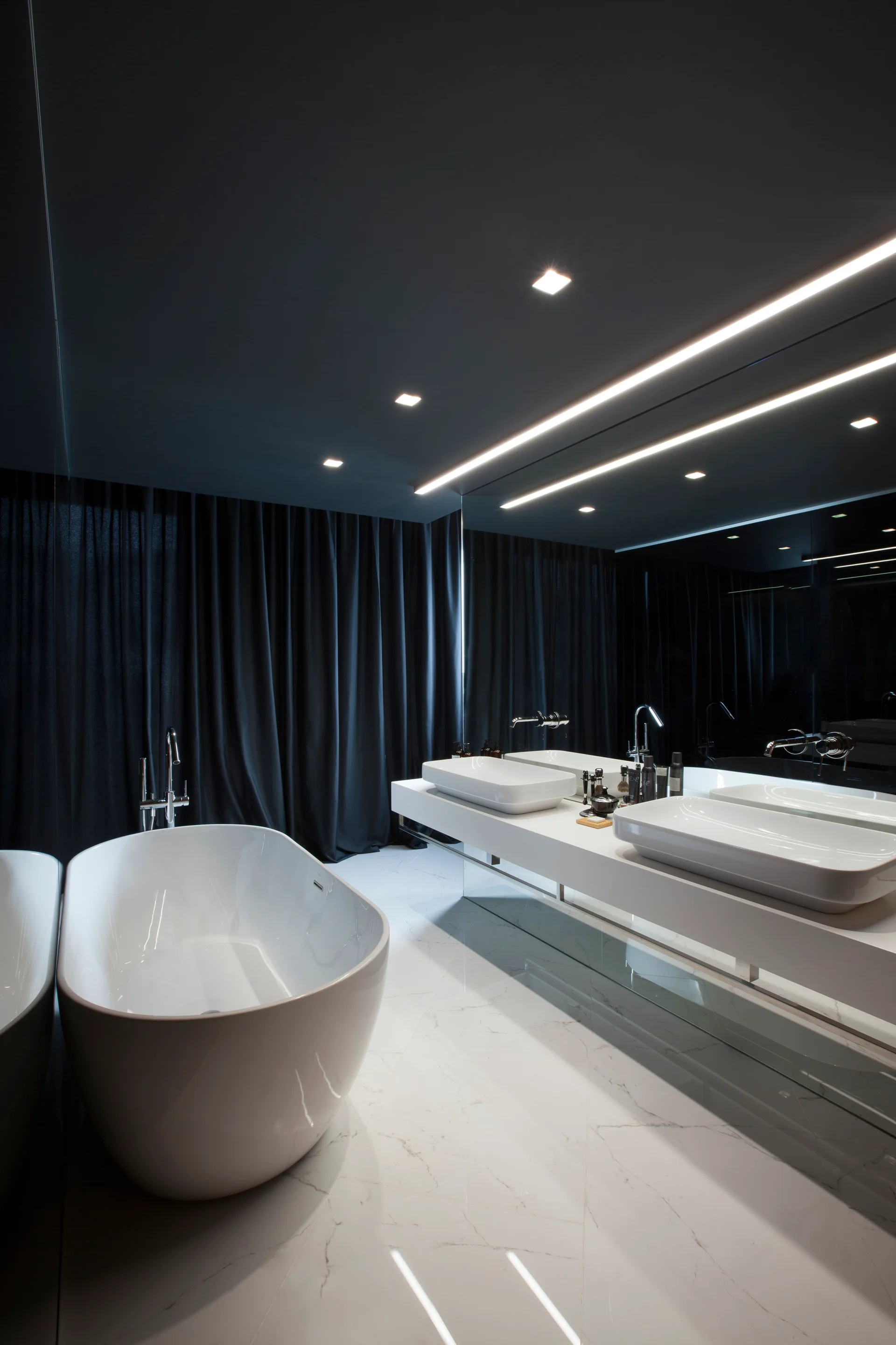 A modern black and white bathroom featuring a white freestanding bathtub, a floating double vanity with vessel sinks, and a dark ceiling.