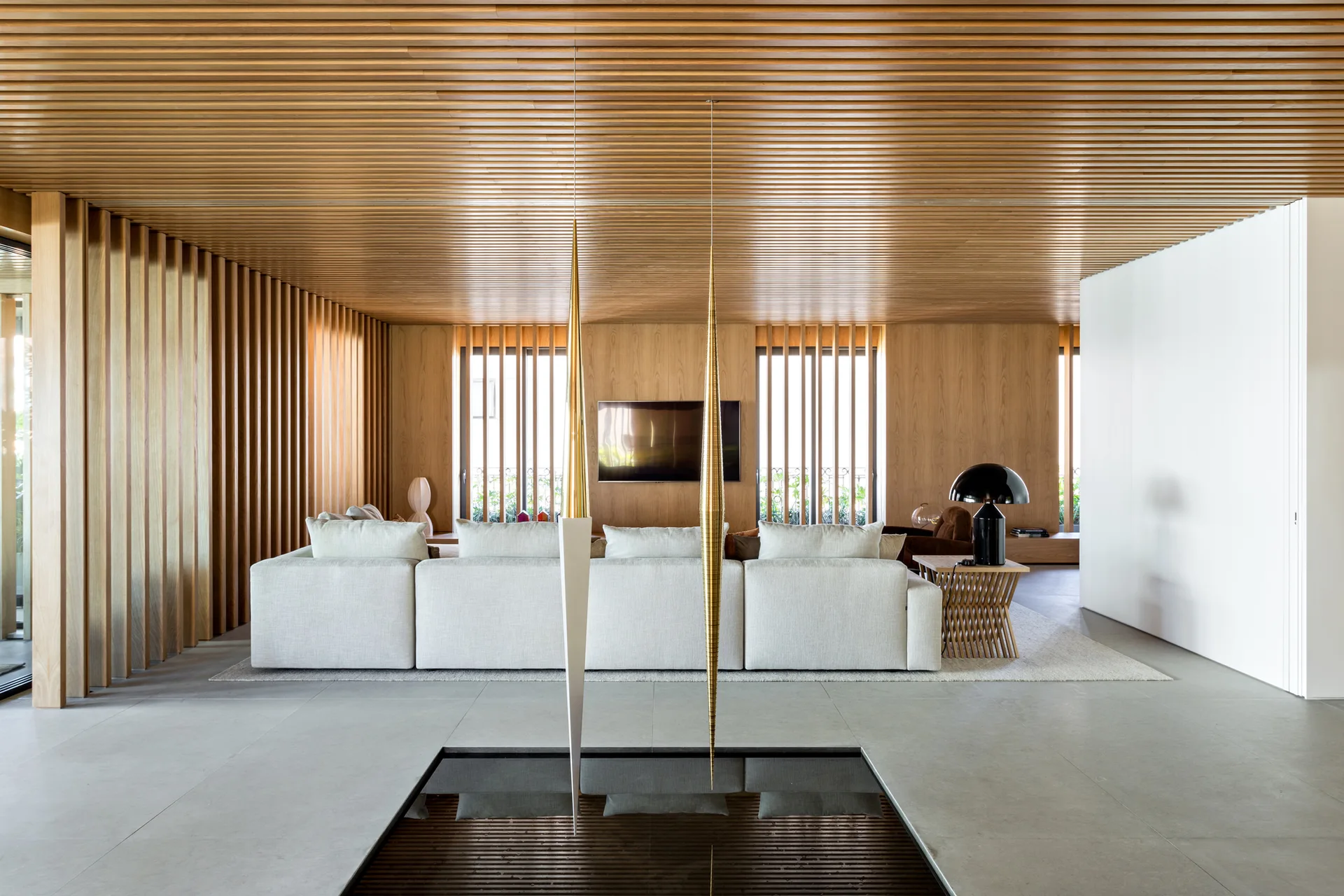 A modern living room features a wooden slat ceiling and walls, a cream modular sofa, and a reflective indoor water feature in the grey tiled floor.