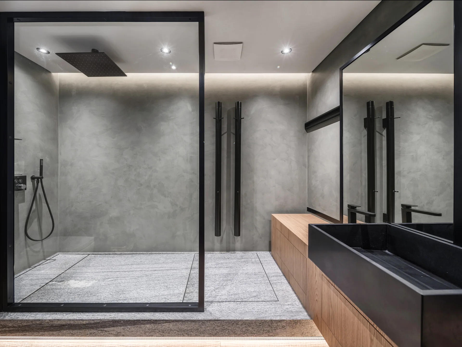 A modern minimalist bathroom with a walk-in glass shower, concrete-effect plaster walls, and a floating wood vanity with a black sink.