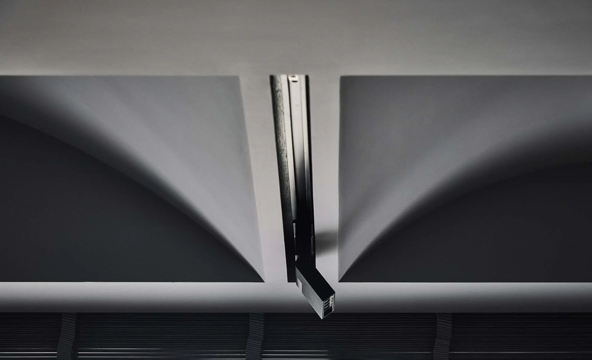A close-up view of a black adjustable track spotlight recessed into a linear channel between white vaulted plaster ceiling arches.