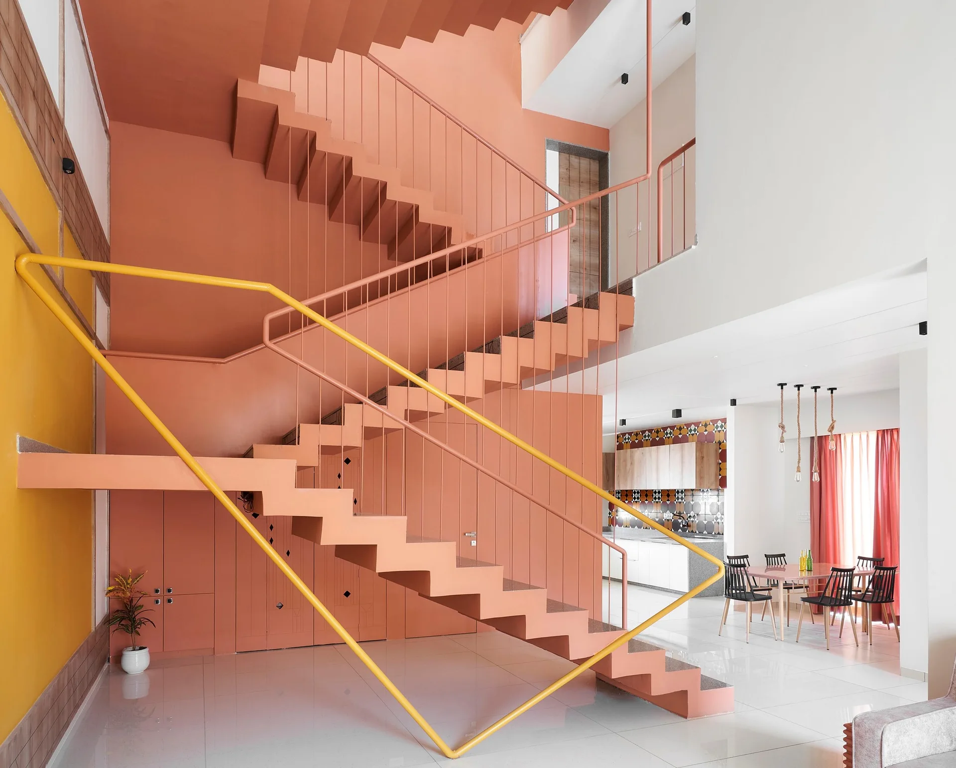 A contemporary peach-colored staircase features a bold yellow railing, set against a polished white tile floor with a dining area visible in the background.