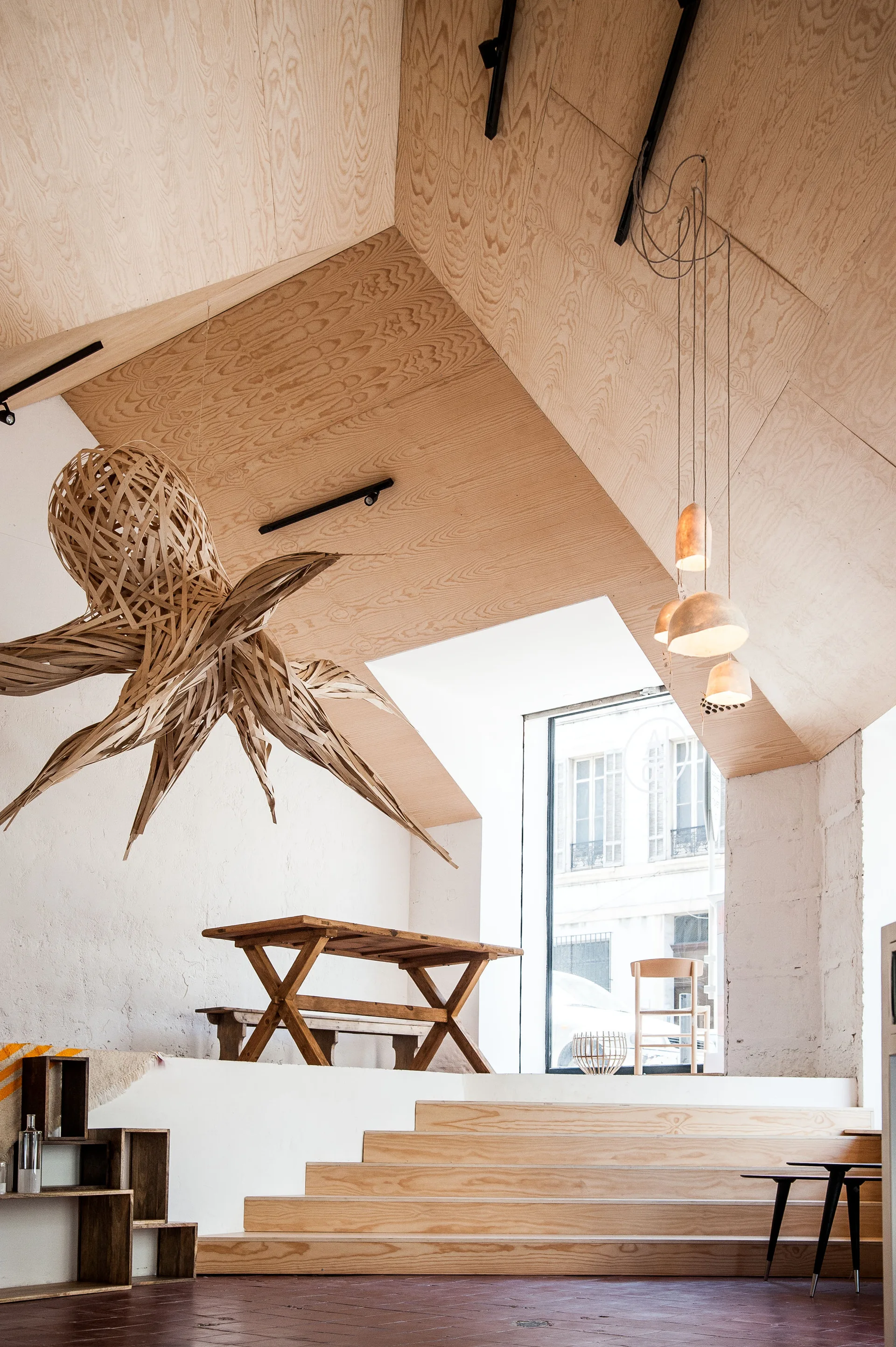 A split-level dining area features wooden steps leading up to a rustic table beneath a sloped plywood ceiling and a large octopus-shaped sculpture.