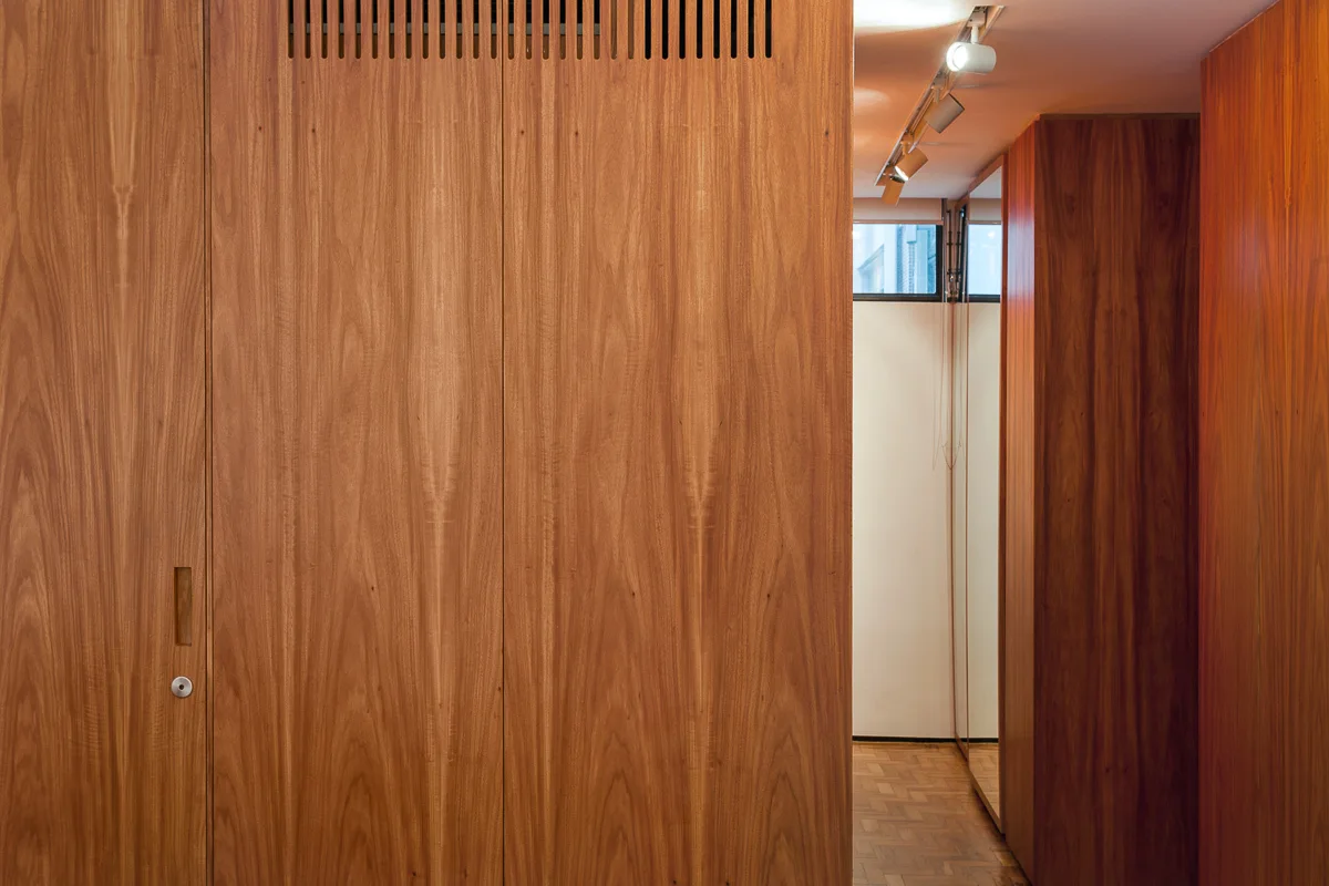 A modern hallway featuring floor-to-ceiling wood cabinetry with vertical vent slats and a warm parquet floor under track lighting.