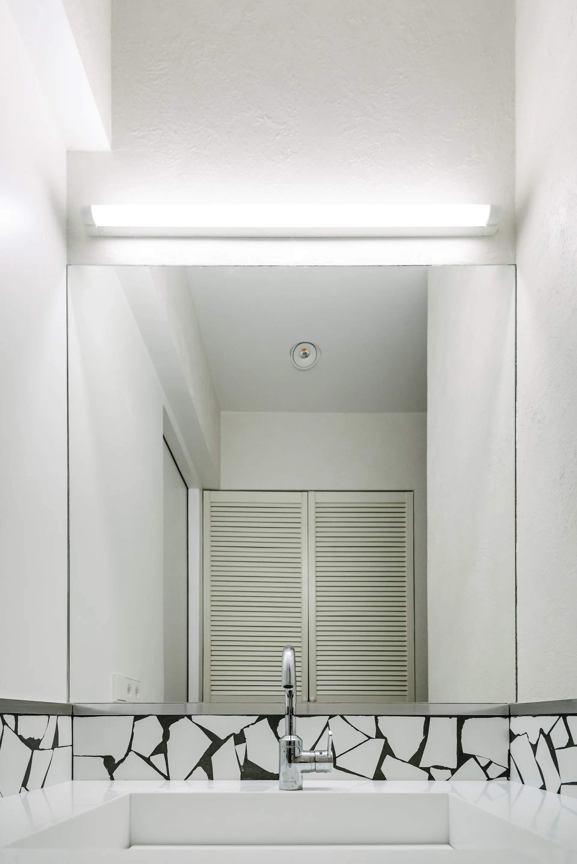 A modern bathroom vanity featuring an integrated white sink, a chrome faucet, and a black and white fragmented mosaic tile backsplash.