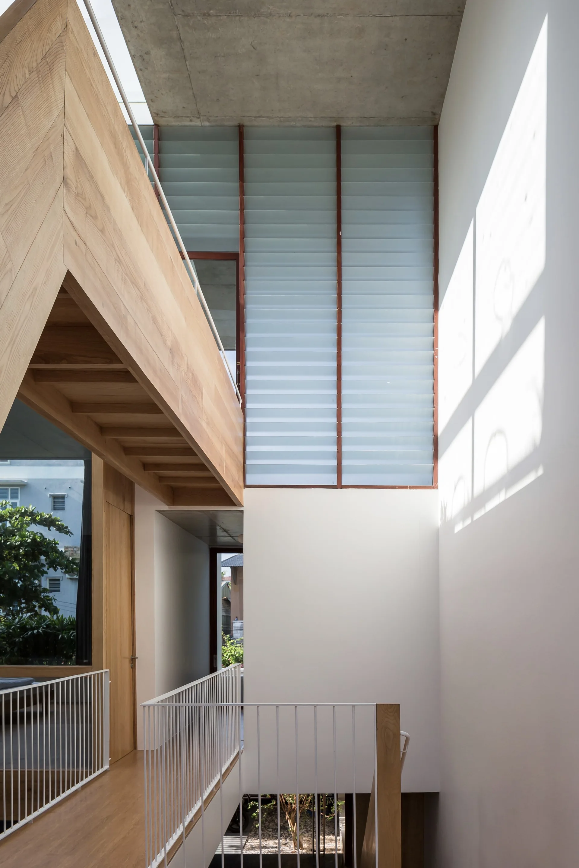 A modern stair landing features warm wood cladding, white metal railings, a raw concrete ceiling, and tall frosted louvered glass windows.