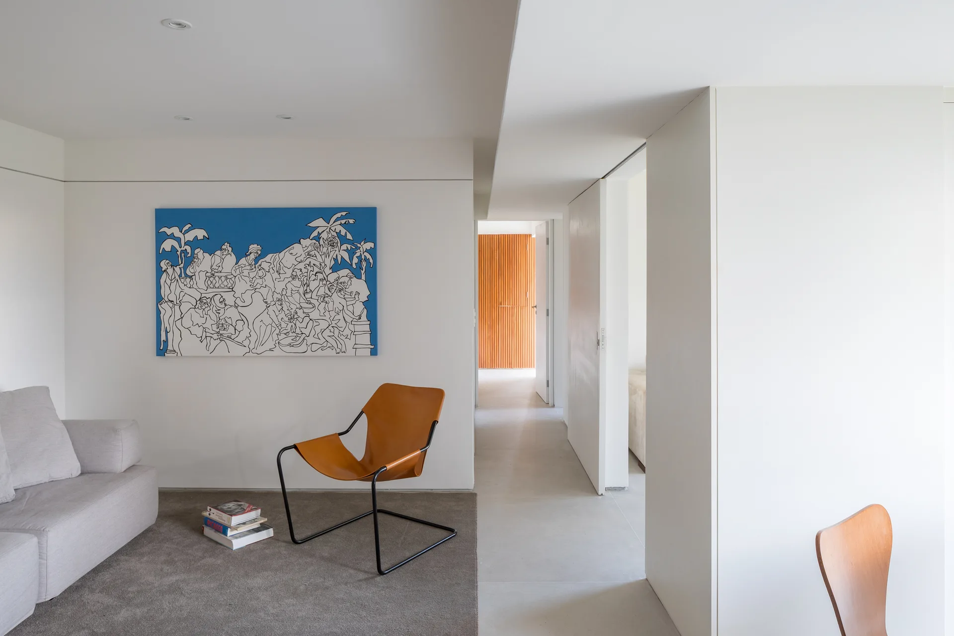 A minimalist white living room with a light grey sofa, a tan leather sling chair, and a large blue painting on the wall.