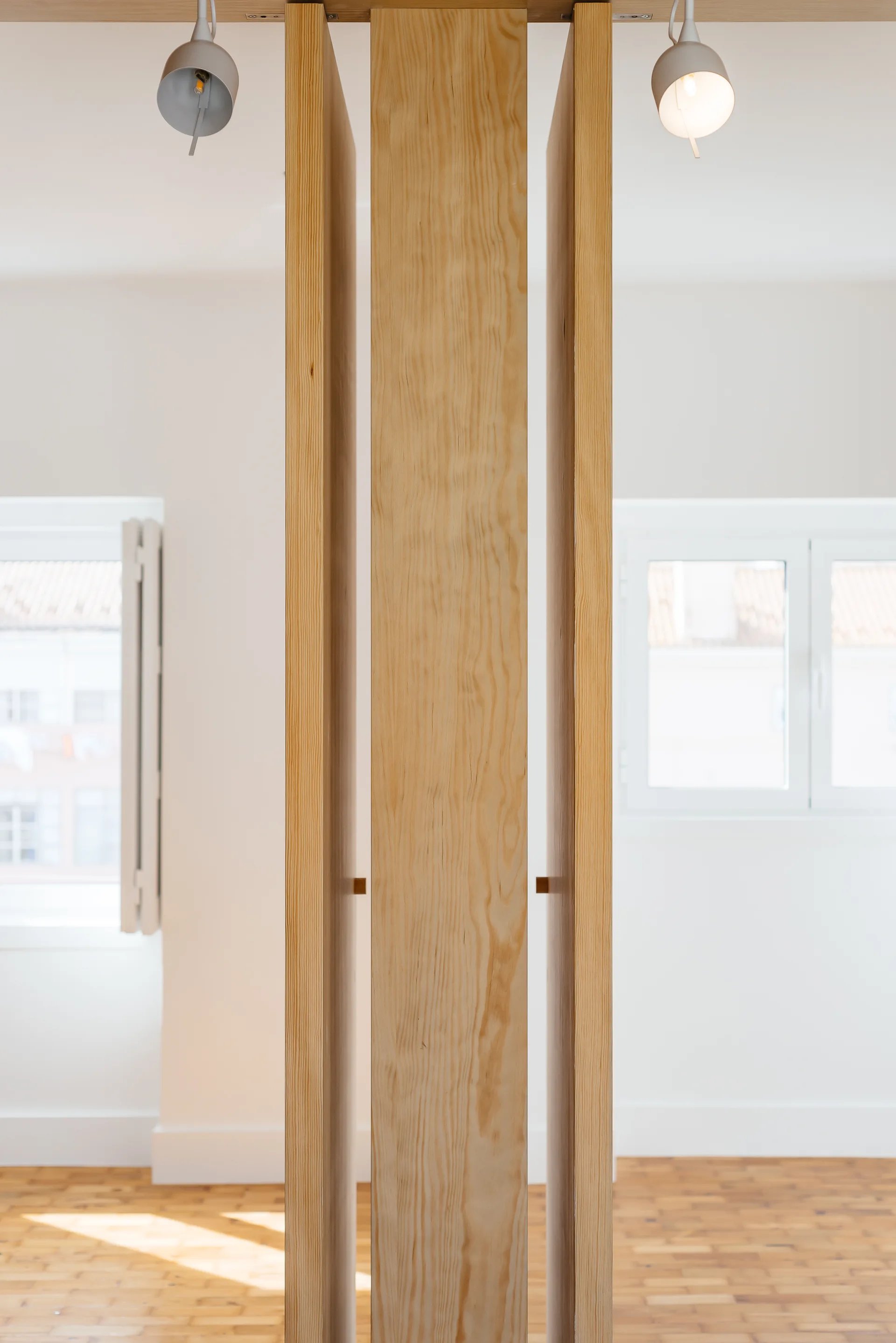 A minimalist room divider crafted from vertical light wood planks set in a bright space with white walls and parquet flooring.