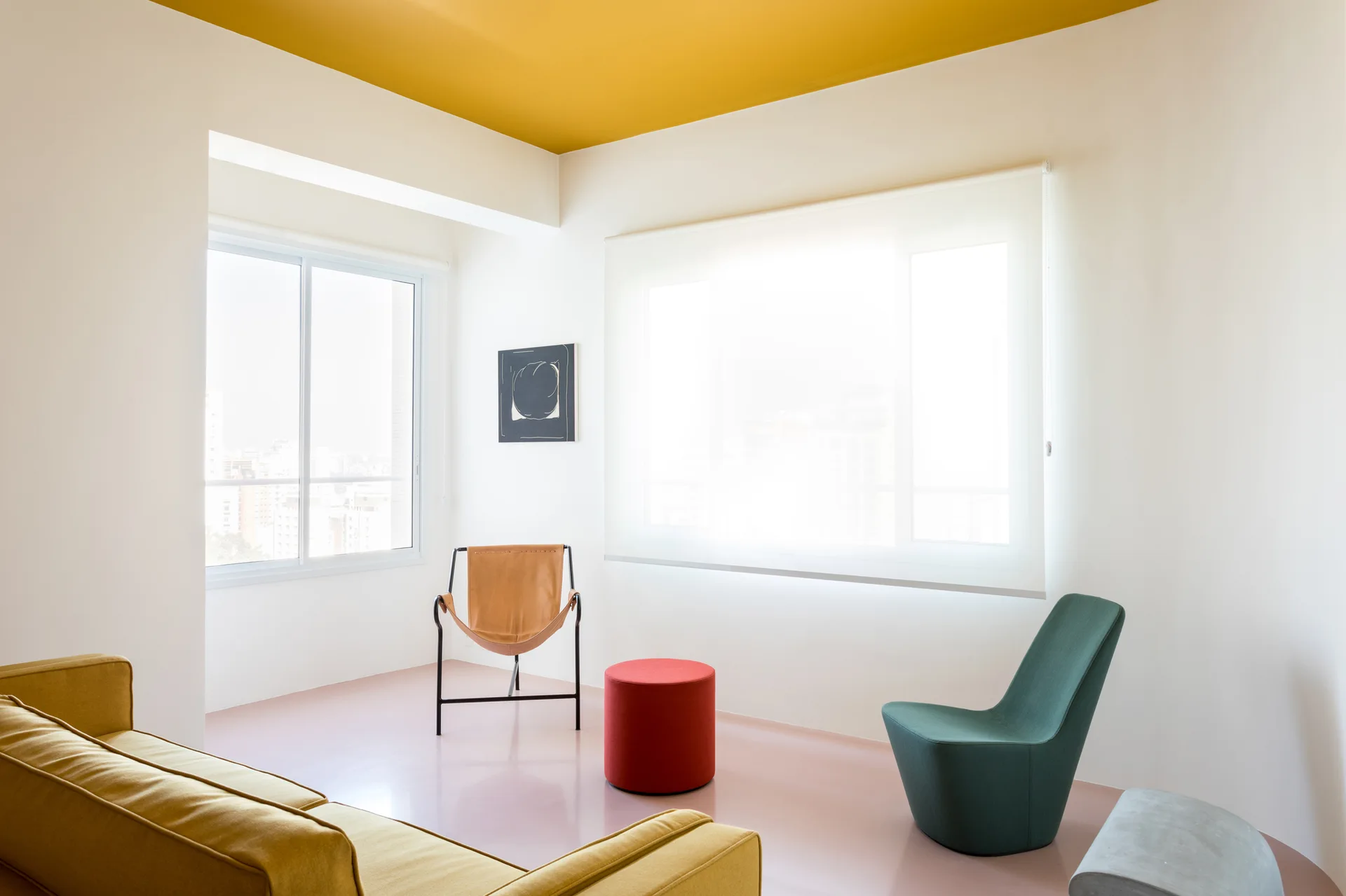 A minimalist living room with a painted yellow ceiling, glossy pink floor, a mustard yellow sofa, and colorful modern chairs near two bright windows.