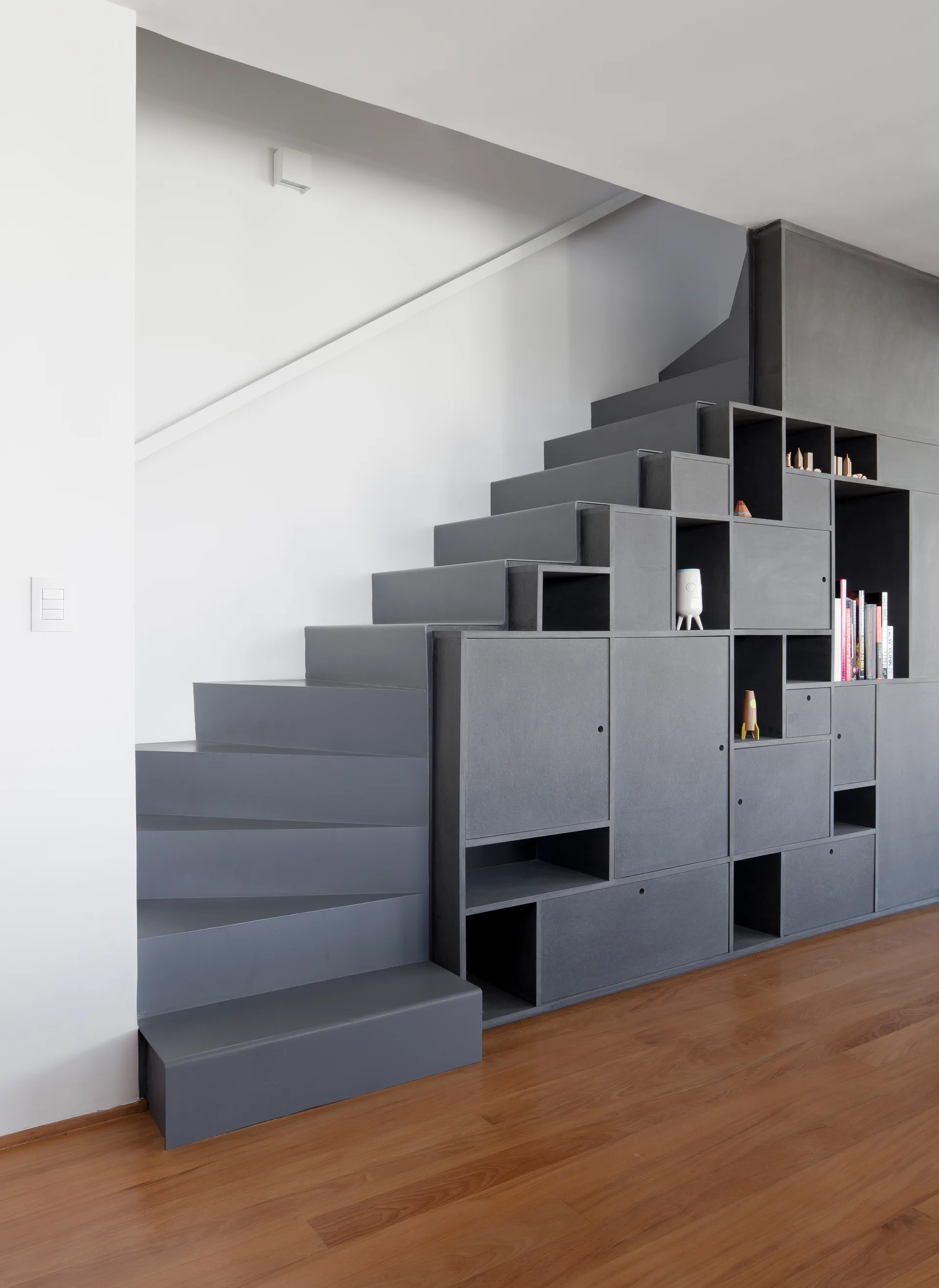 A dark grey minimalist staircase featuring integrated modular storage compartments and open shelves set against a white wall.