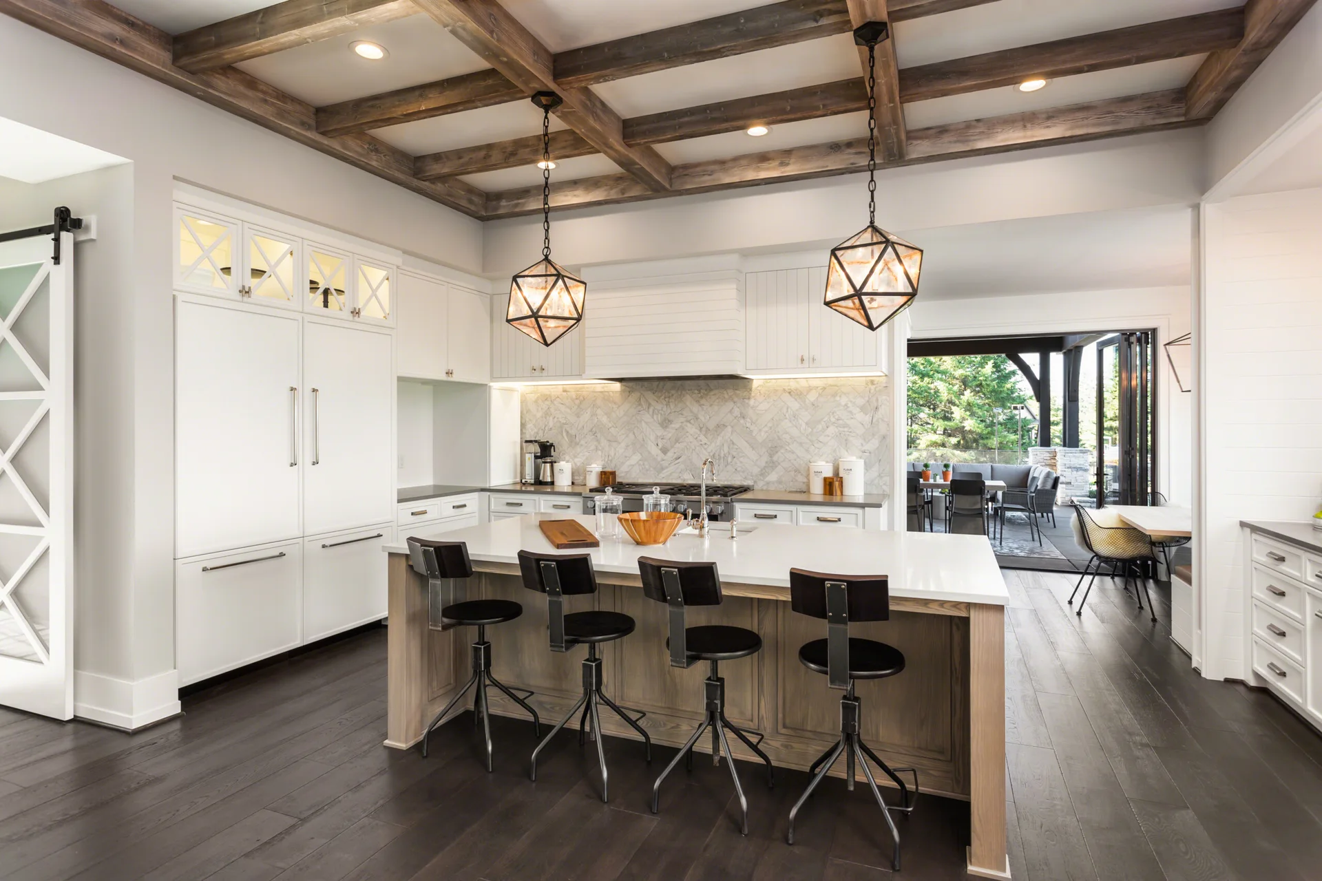 A spacious kitchen featuring a central wood-paneled island, dark metal bar stools, white cabinetry, and a coffered dark wood ceiling.