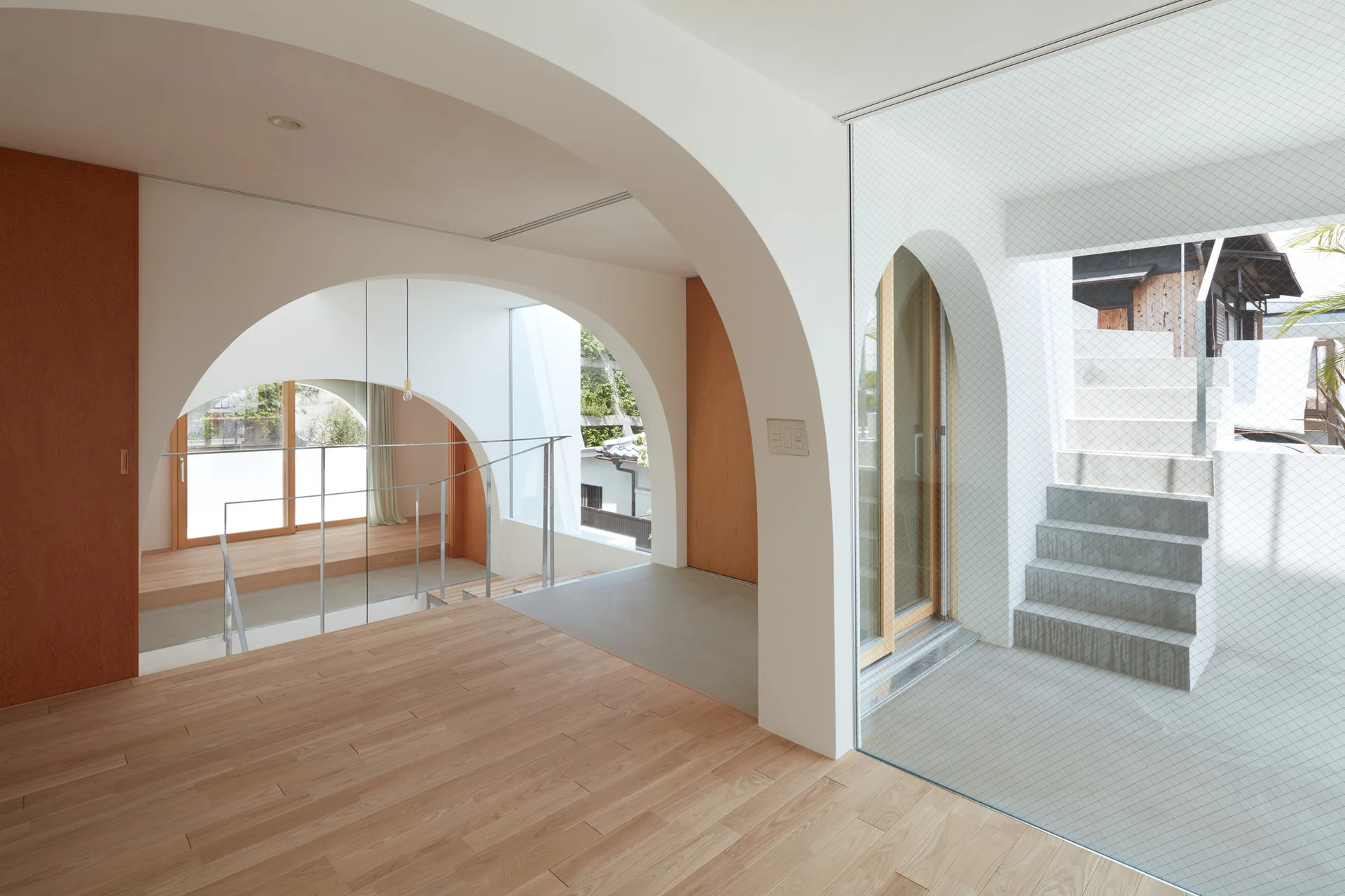 A minimalist interior featuring smooth white plaster arches, light wood floors, and a concrete staircase viewed through glass.