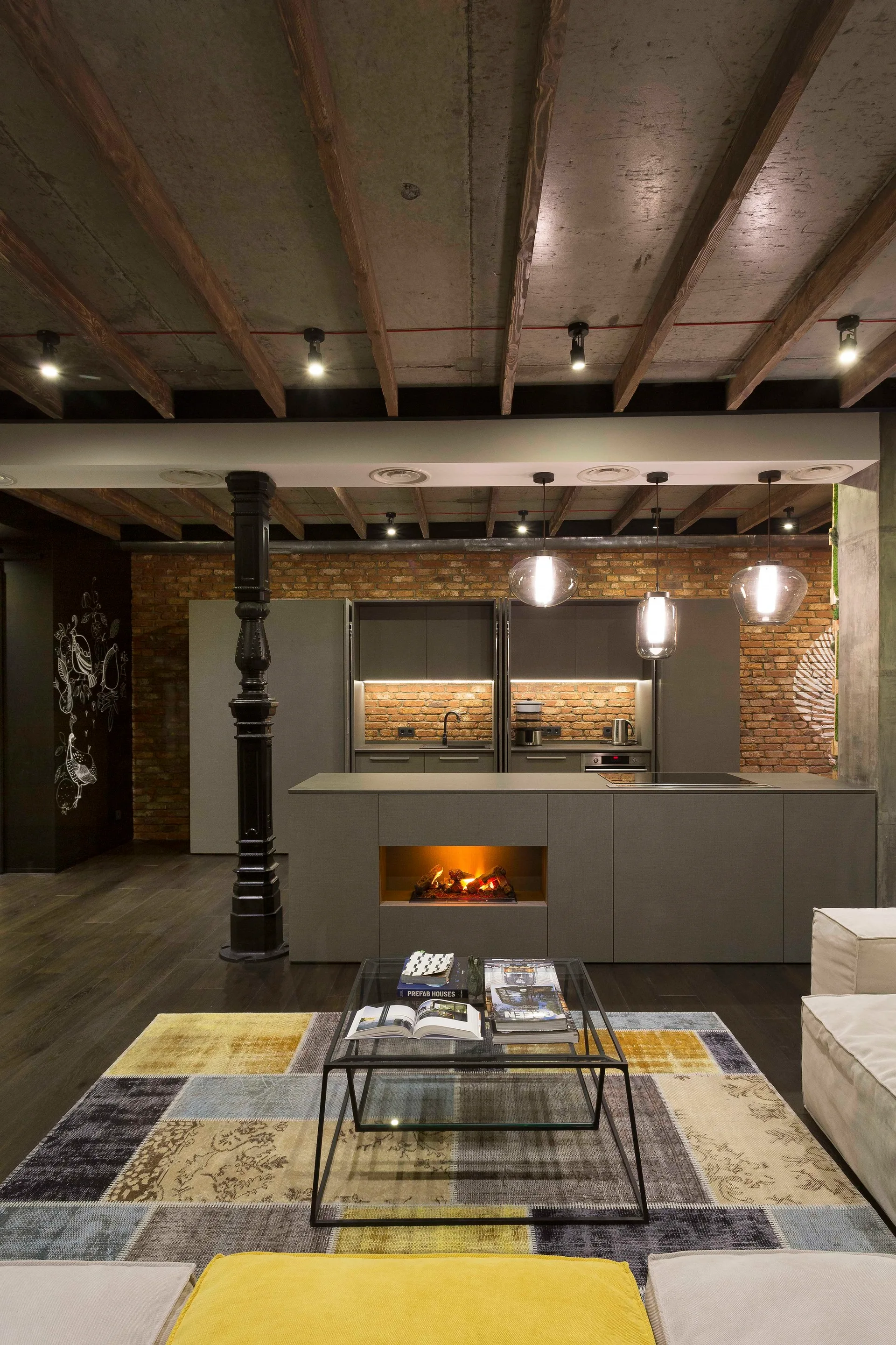 An industrial style open plan kitchen featuring a matte gray island with a built-in fireplace against an exposed brick wall.