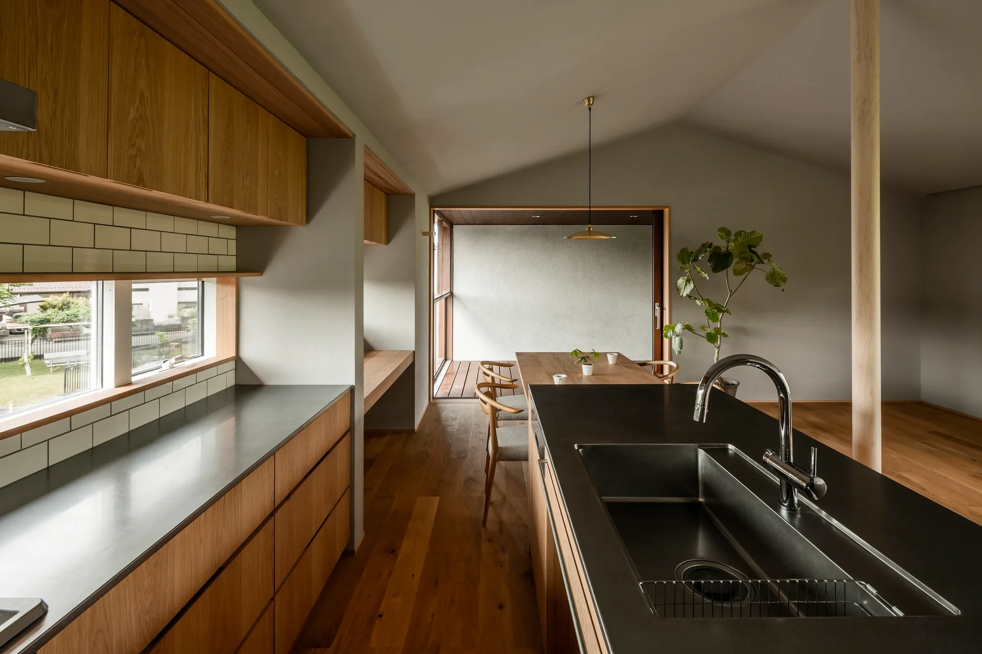 A modern kitchen and dining area featuring warm oak cabinetry, a matte black island with a sink, and a wooden dining table under a sloped ceiling.
