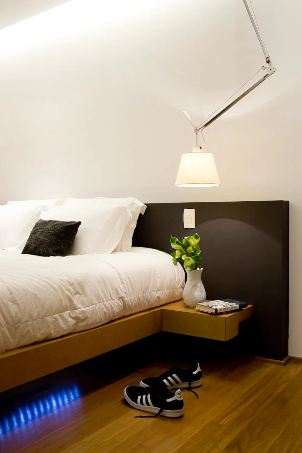 A modern bedroom features a platform bed with white bedding, a dark brown wall panel headboard, and an attached floating wooden nightstand.