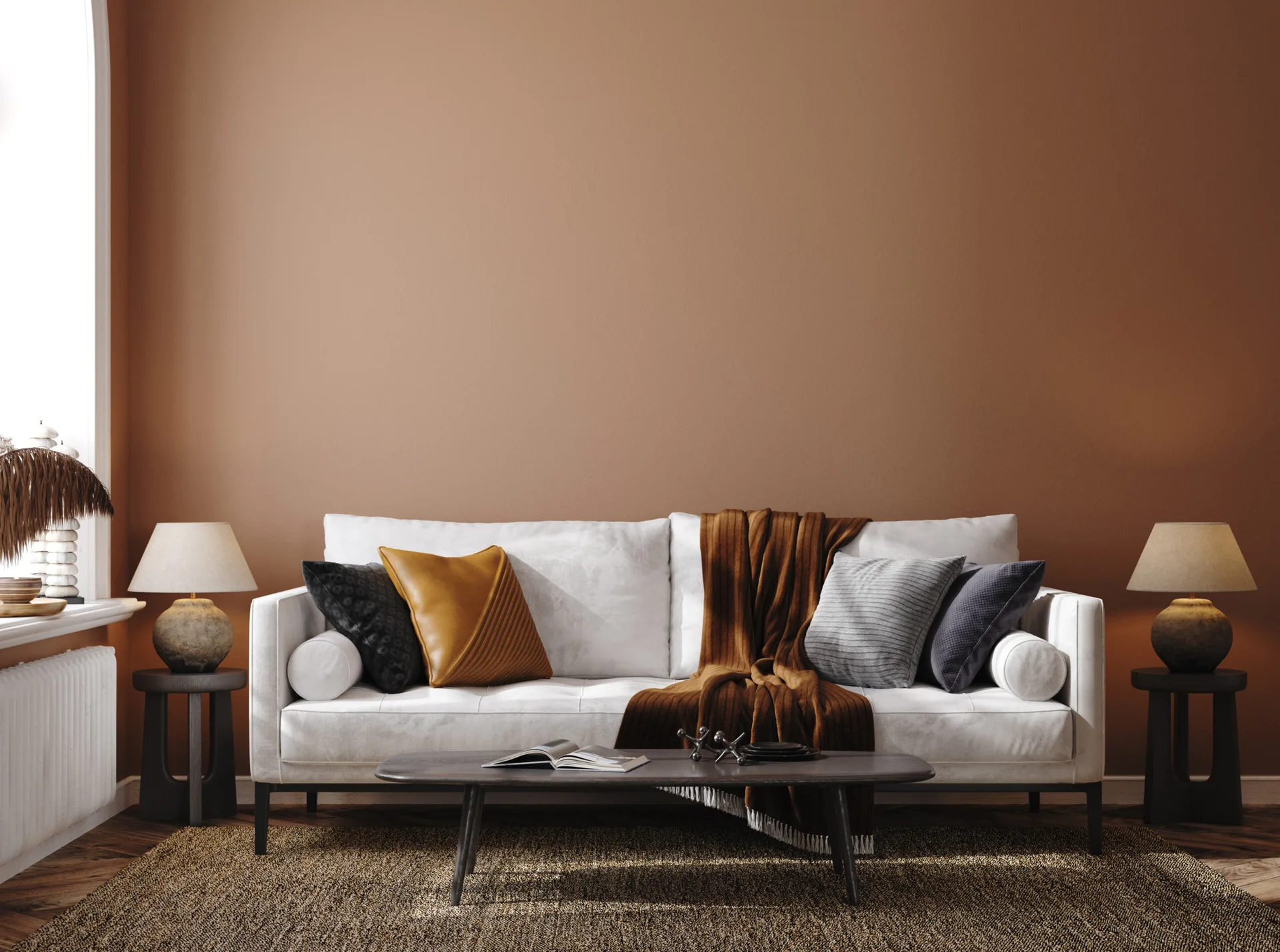 A white upholstered sofa sits against a terracotta painted wall, flanked by two matching side tables with warm lamps in a symmetrical living room.