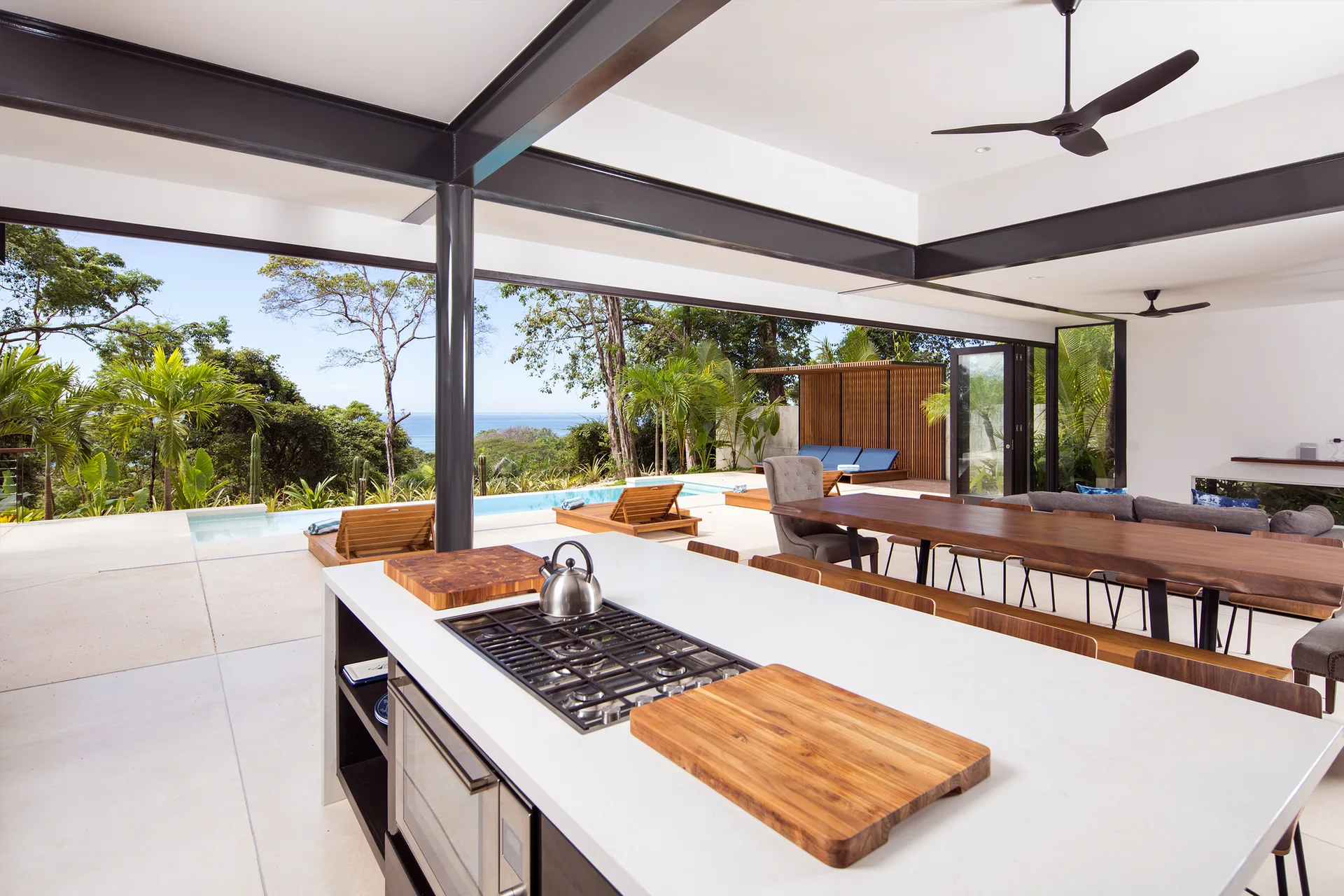 An open-concept kitchen with a white-topped island and a long wood dining table opening directly to an outdoor pool deck.