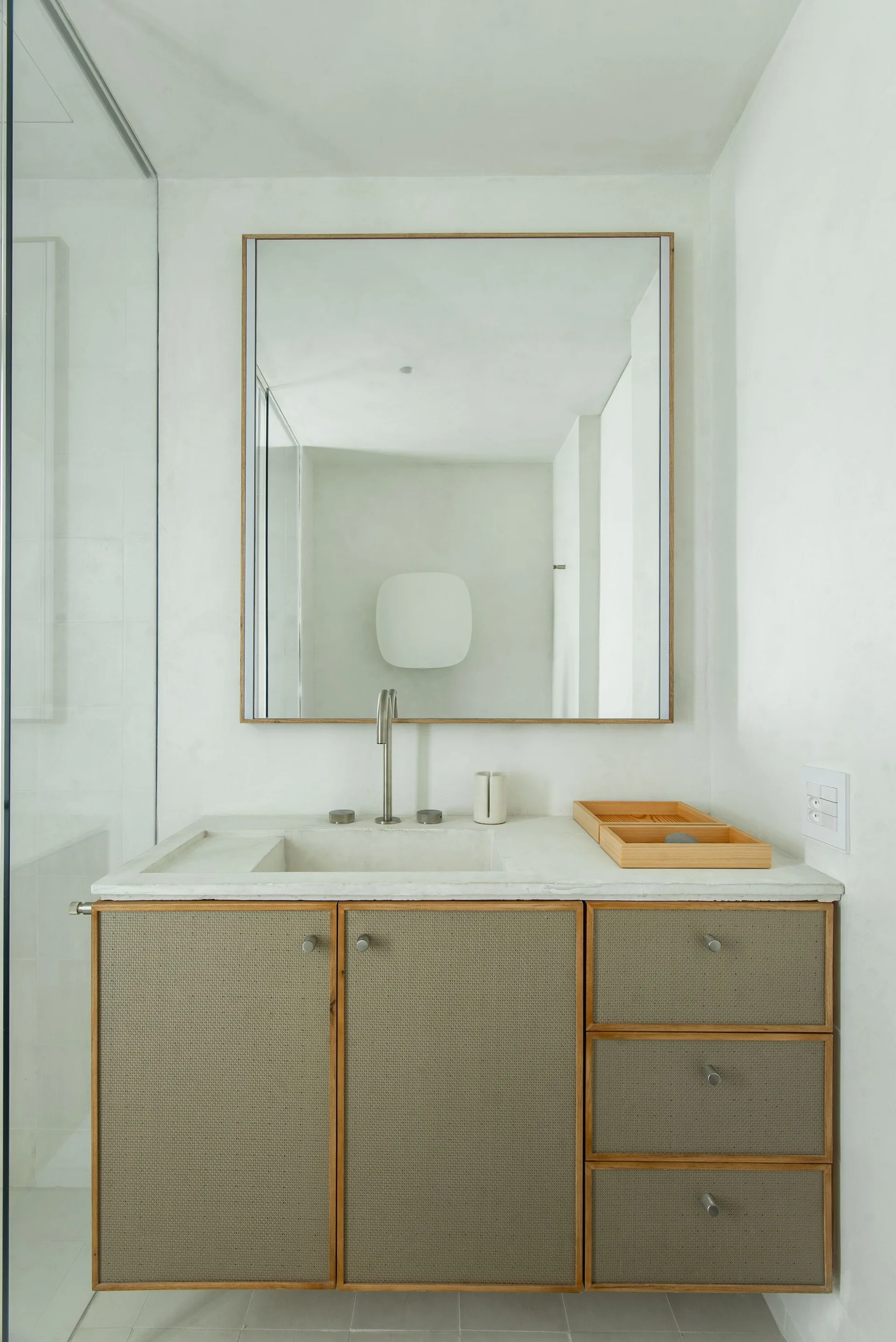 A minimalist bathroom vanity with woven mesh cabinet fronts, an integrated stone sink, a brushed metal faucet, and a large wood-framed mirror.