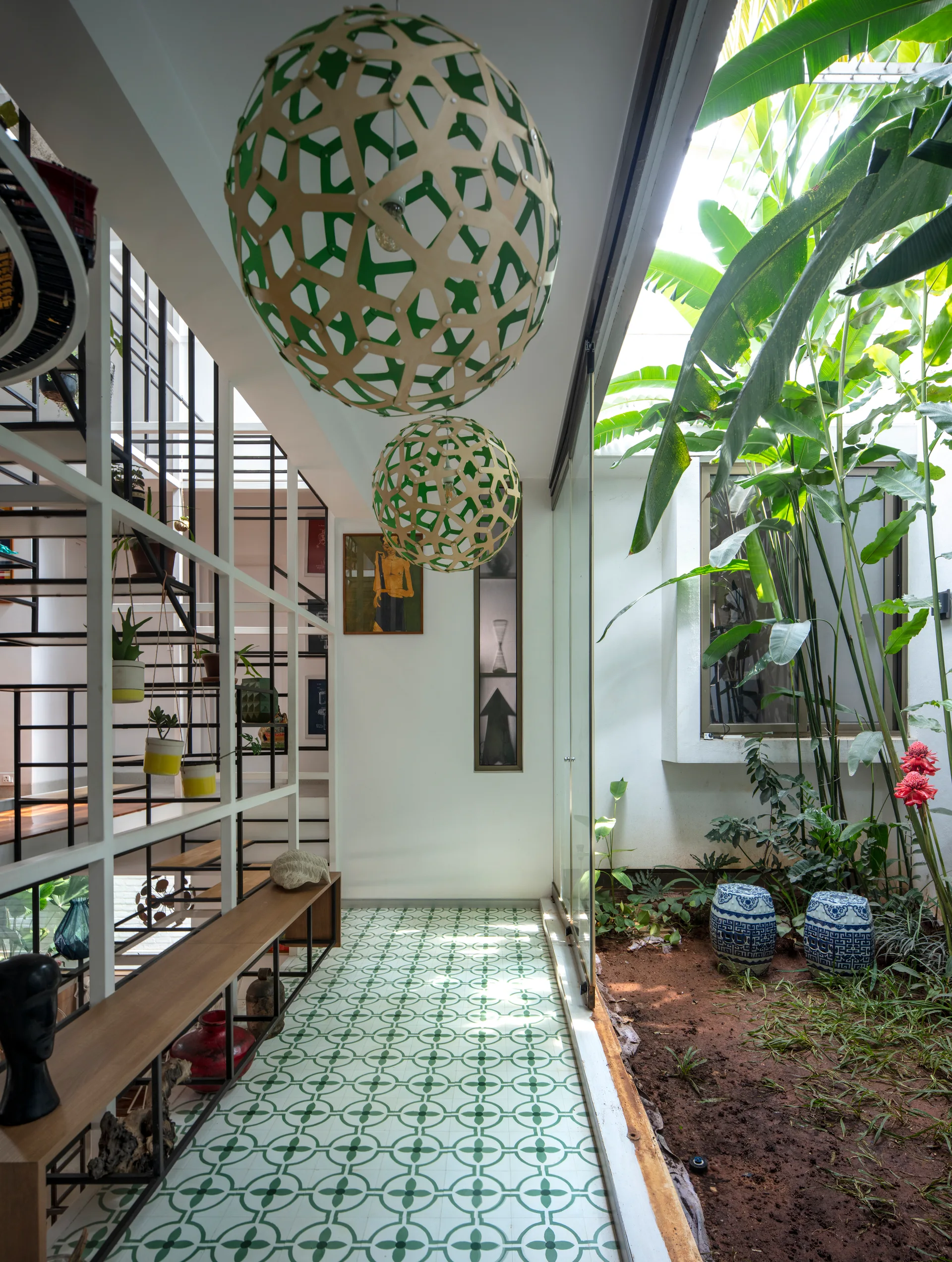 A hallway features green patterned floor tiles, spherical pendant lights, and a glass wall looking into a courtyard garden.