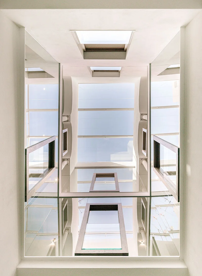 A low-angle shot looking up a white light well with a central rectangular skylight and mirrored side walls reflecting the blue sky.