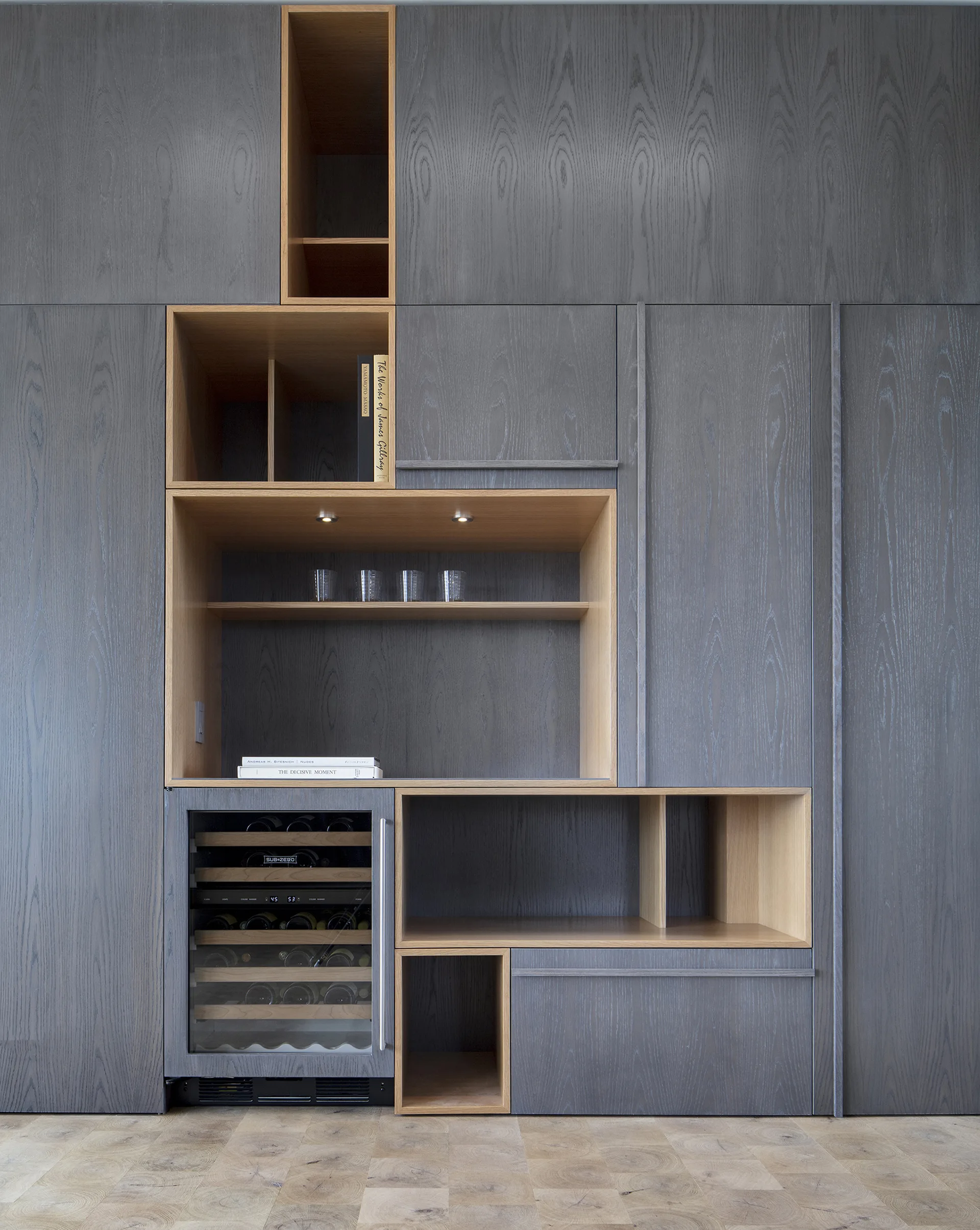 A floor-to-ceiling gray wood cabinet unit features open natural wood shelves and a built-in wine cooler above parquet floors.