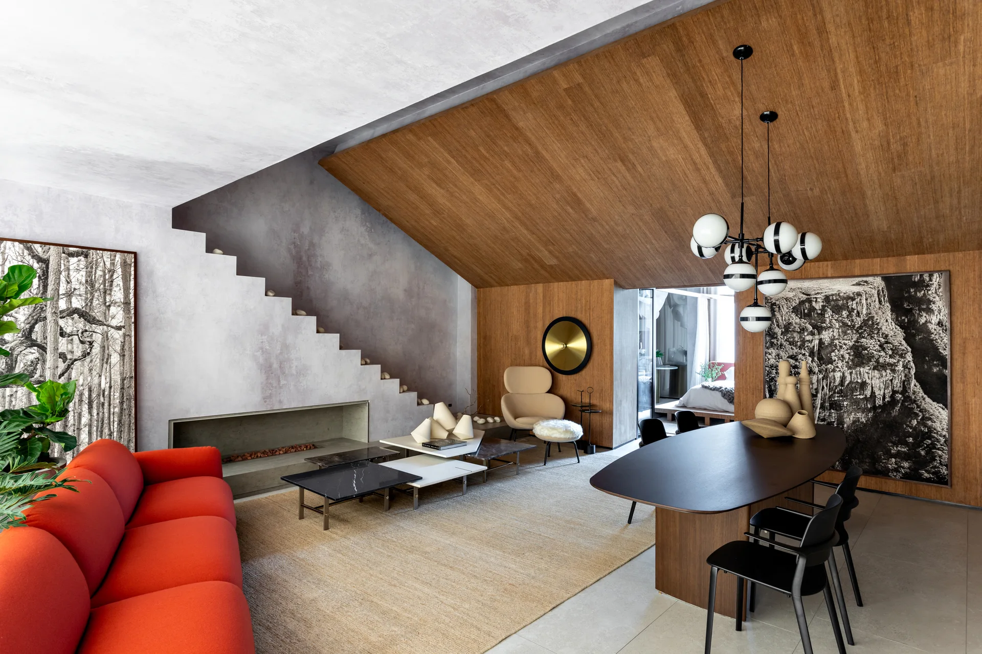 A modern open-plan living and dining area featuring a vibrant red sofa, a sloped wood-paneled ceiling, an integrated plaster staircase, and a dining table.