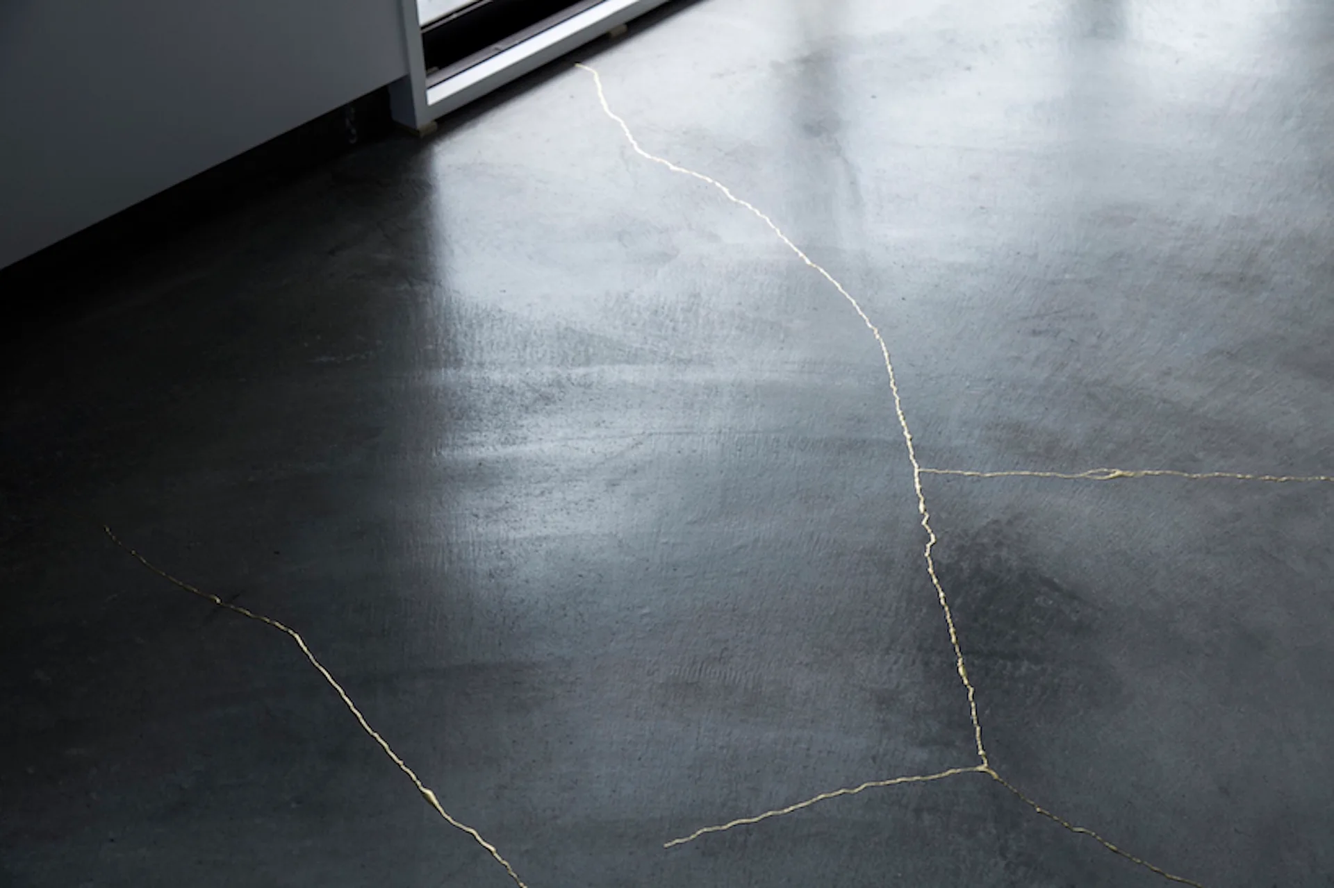 A close-up view of a dark grey concrete floor featuring thin, irregular gold inlay lines that mimic natural cracks.