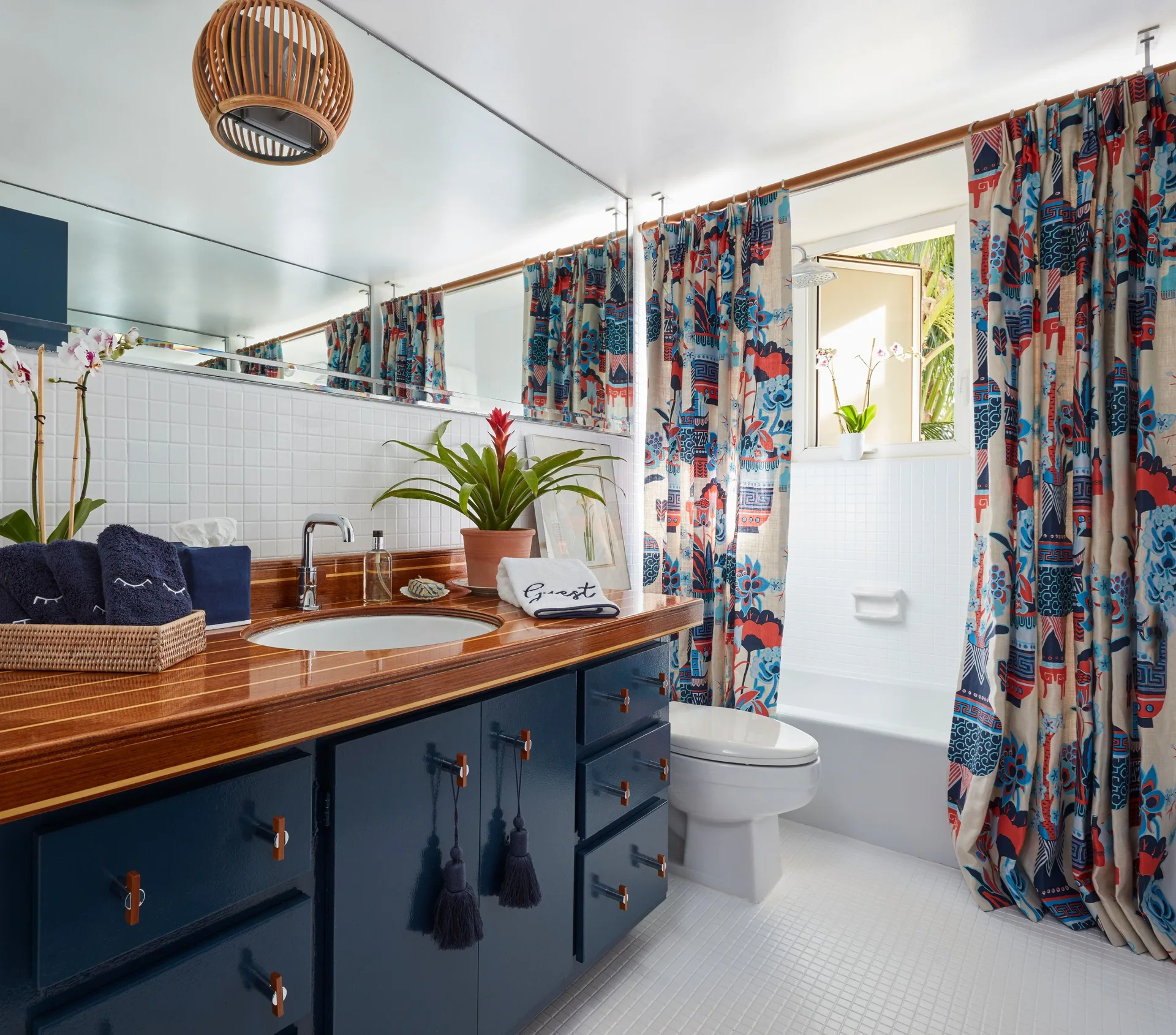 A vibrant bathroom features a glossy blue vanity with a varnished wood countertop, white tiled walls, and patterned shower curtains.