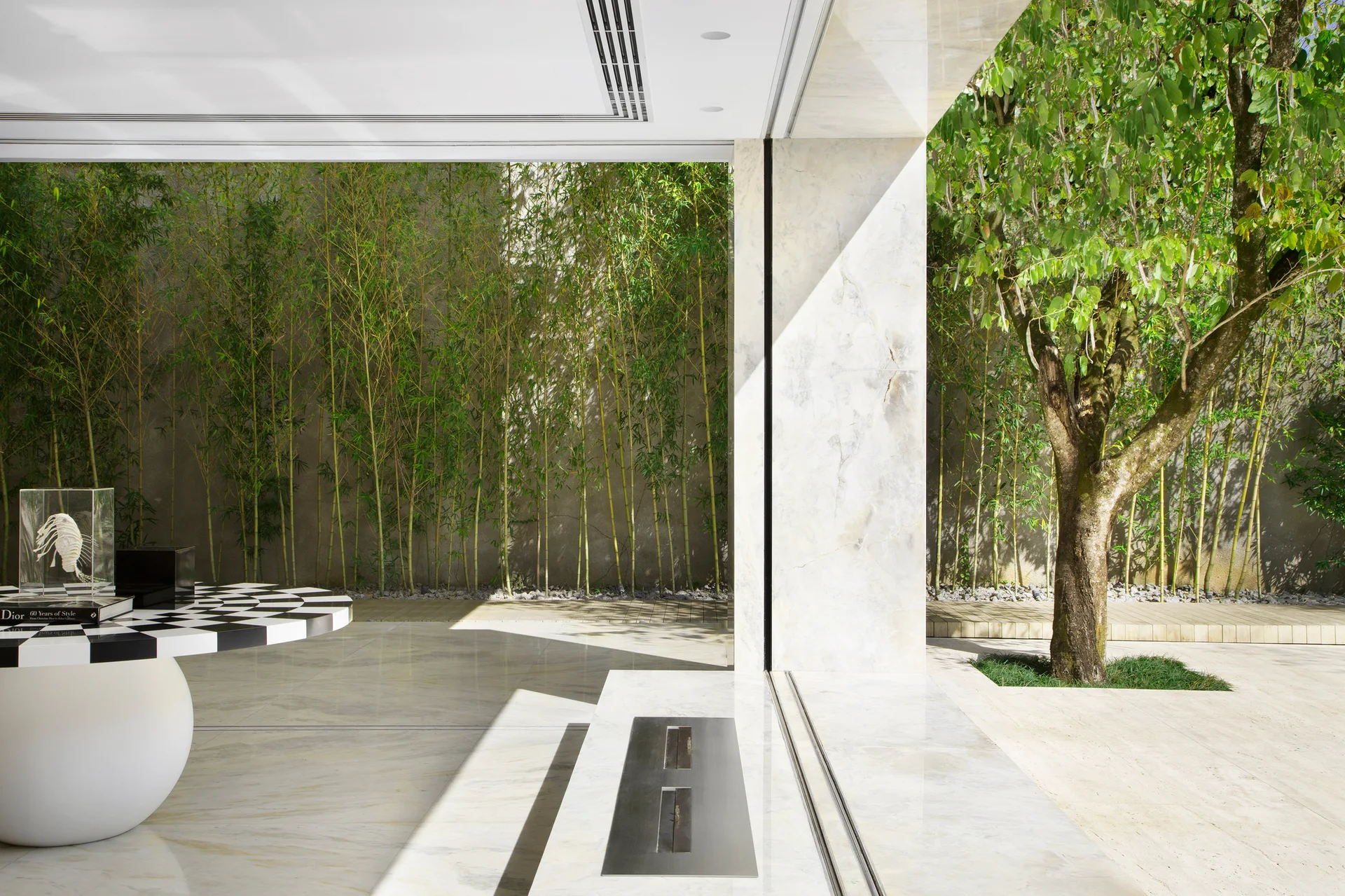 A polished stone patio features a built-in linear fireplace, a black-and-white checkerboard table, and a tall bamboo screen.