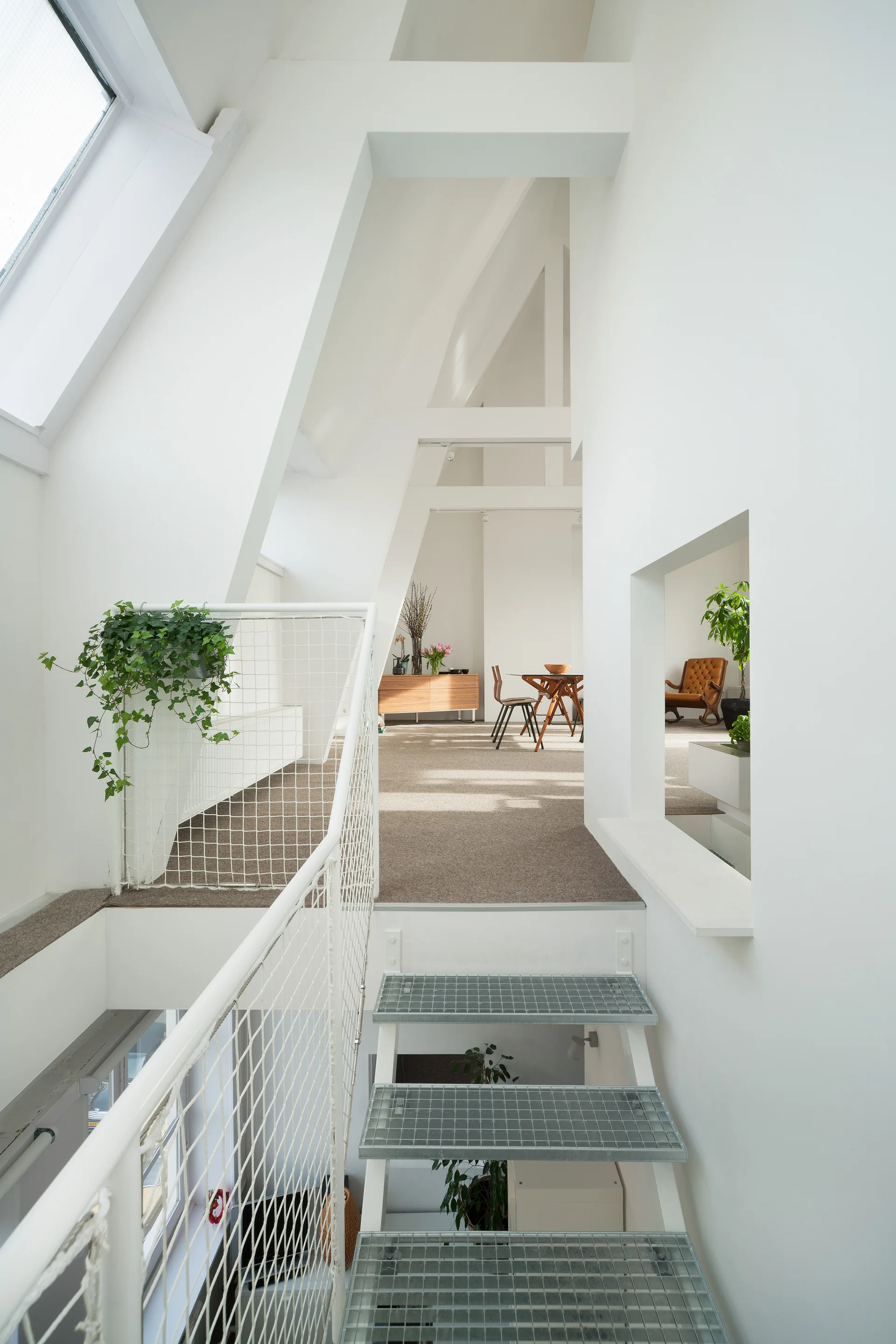 A white metal staircase with grid-patterned treads leads up to an open loft mezzanine with a white mesh railing and skylights.