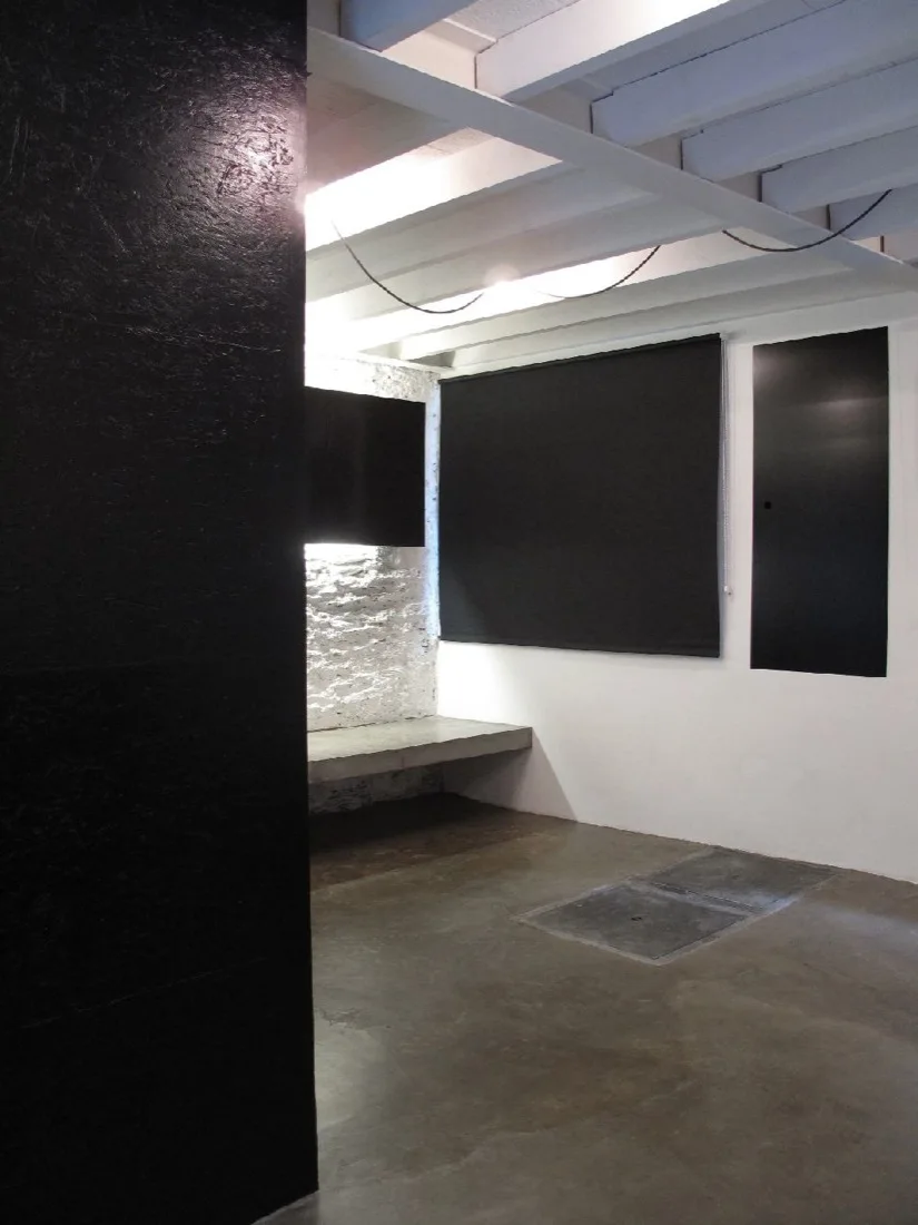 A minimalist space features a polished concrete floor, a white painted brick wall with a built-in concrete bench, and a large black partition.