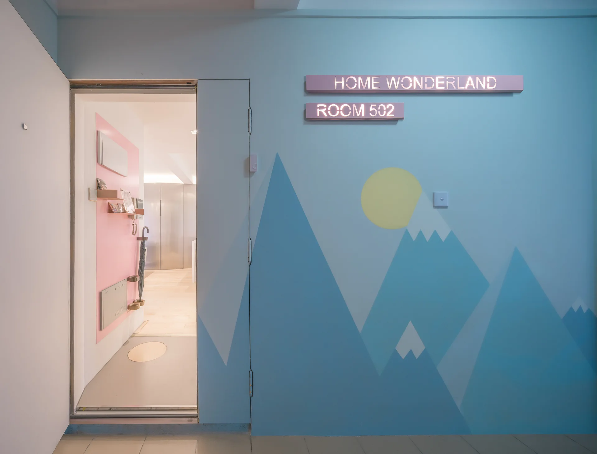 A light blue entryway wall features a painted mountain mural and dimensional room signage next to an open doorway revealing a pink panel.