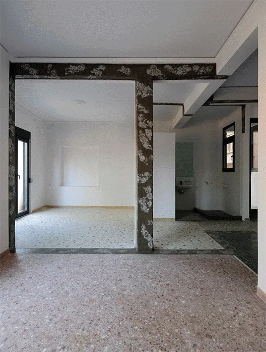 An empty home interior with multi-tonal terrazzo flooring, plain white walls, and dark concrete columns decorated with white floral patterns.