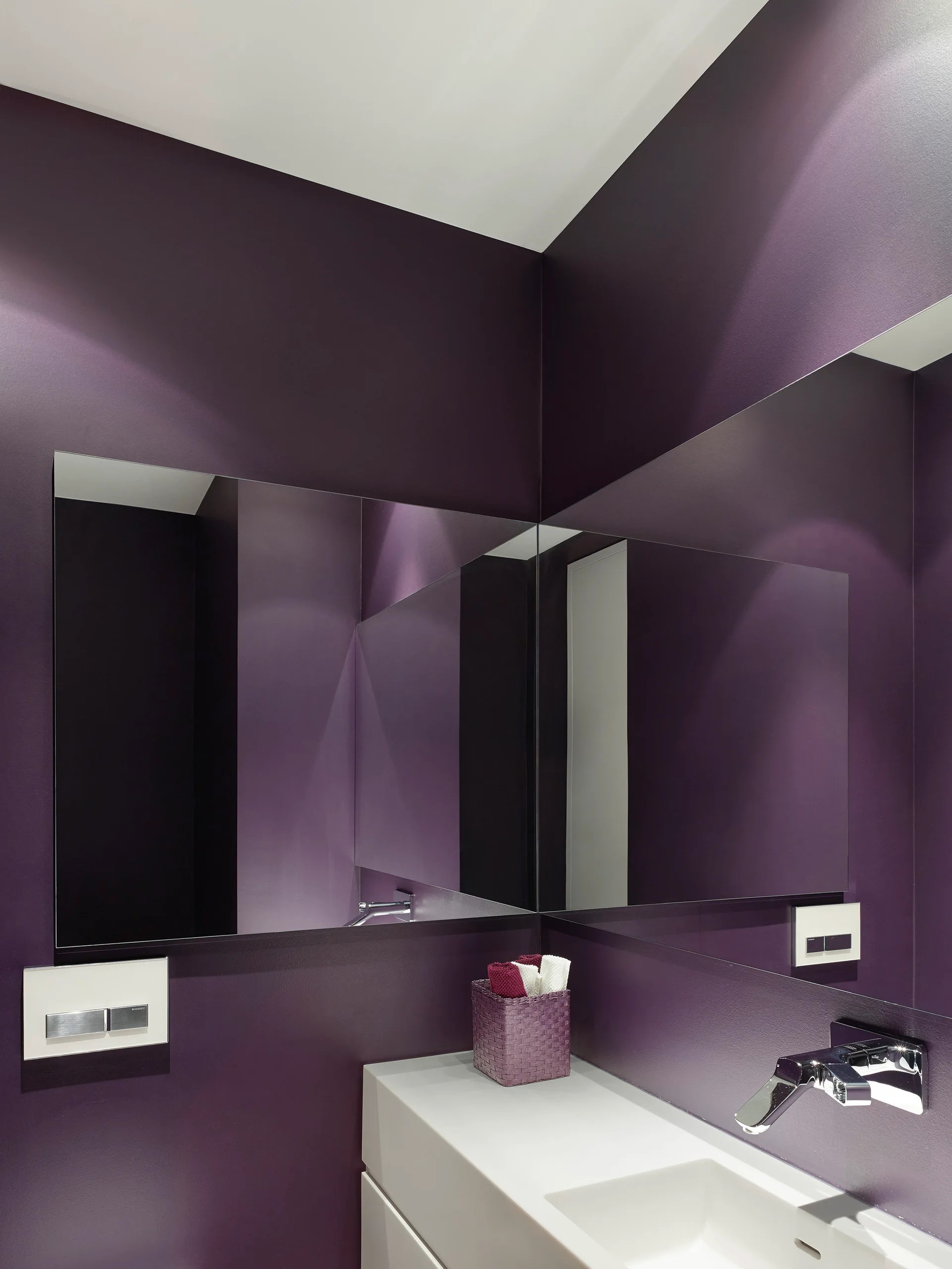 A modern powder room features dark purple walls, a white floating vanity with a chrome wall-mounted faucet, and a large mirror meeting in the corner.