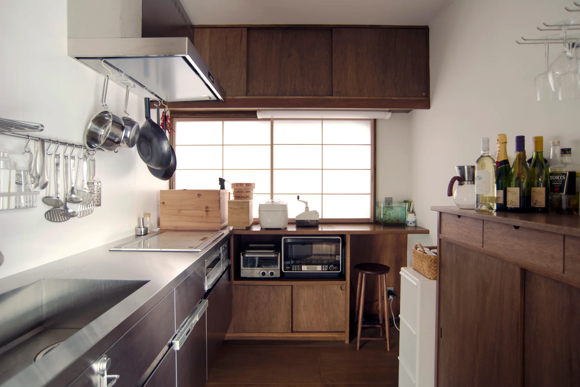 A compact Japanese-style kitchen features dark wood cabinetry, a stainless steel countertop, and a translucent shoji screen window.