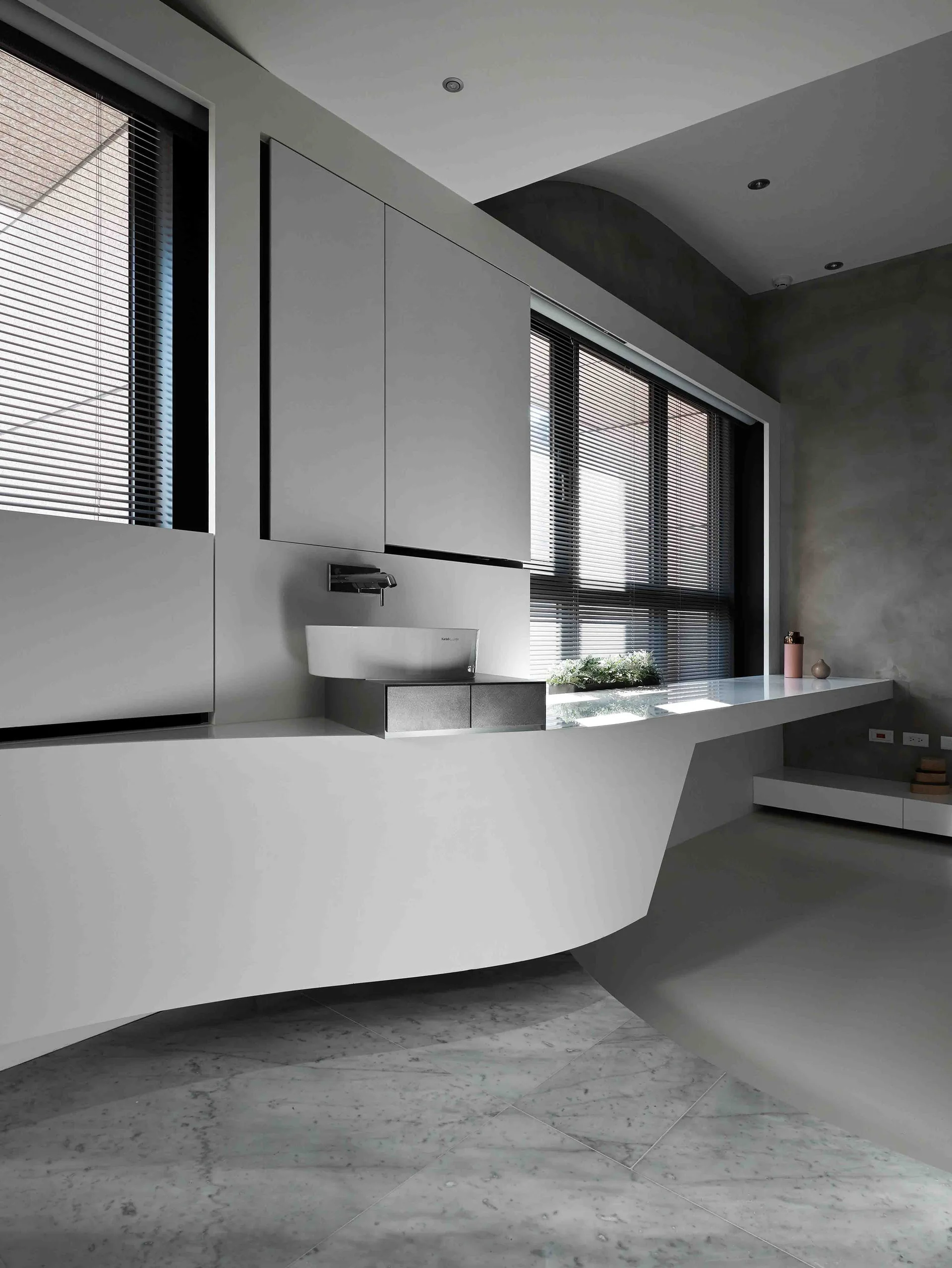 A minimalist modern bathroom featuring a long, cantilevered white vanity, a sleek vessel sink, upper cabinets, and veined marble tile flooring.
