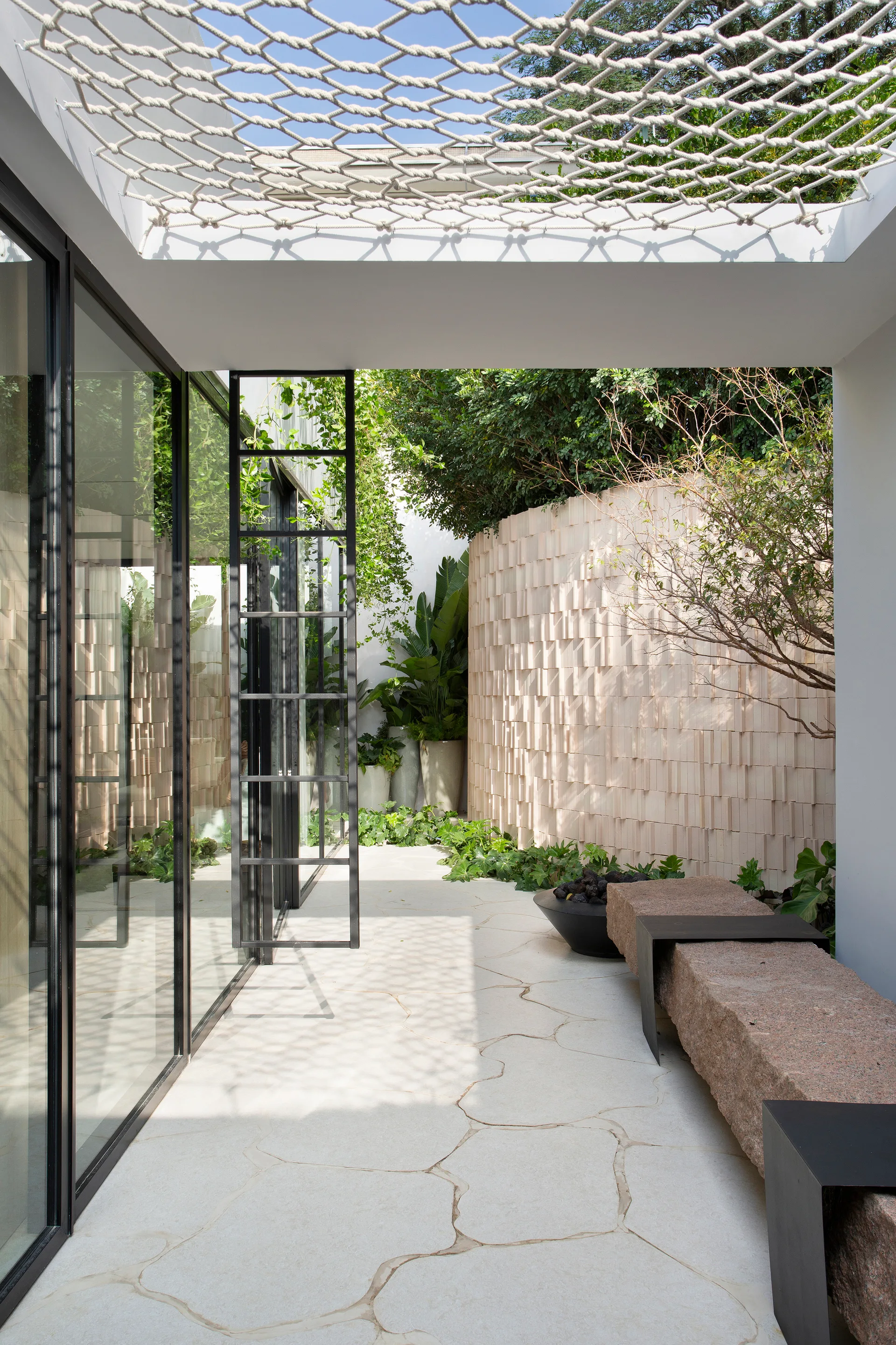 A modern outdoor courtyard with irregular flagstone paving, a long stone bench, a circular fire pit, and a textured curved stone wall.