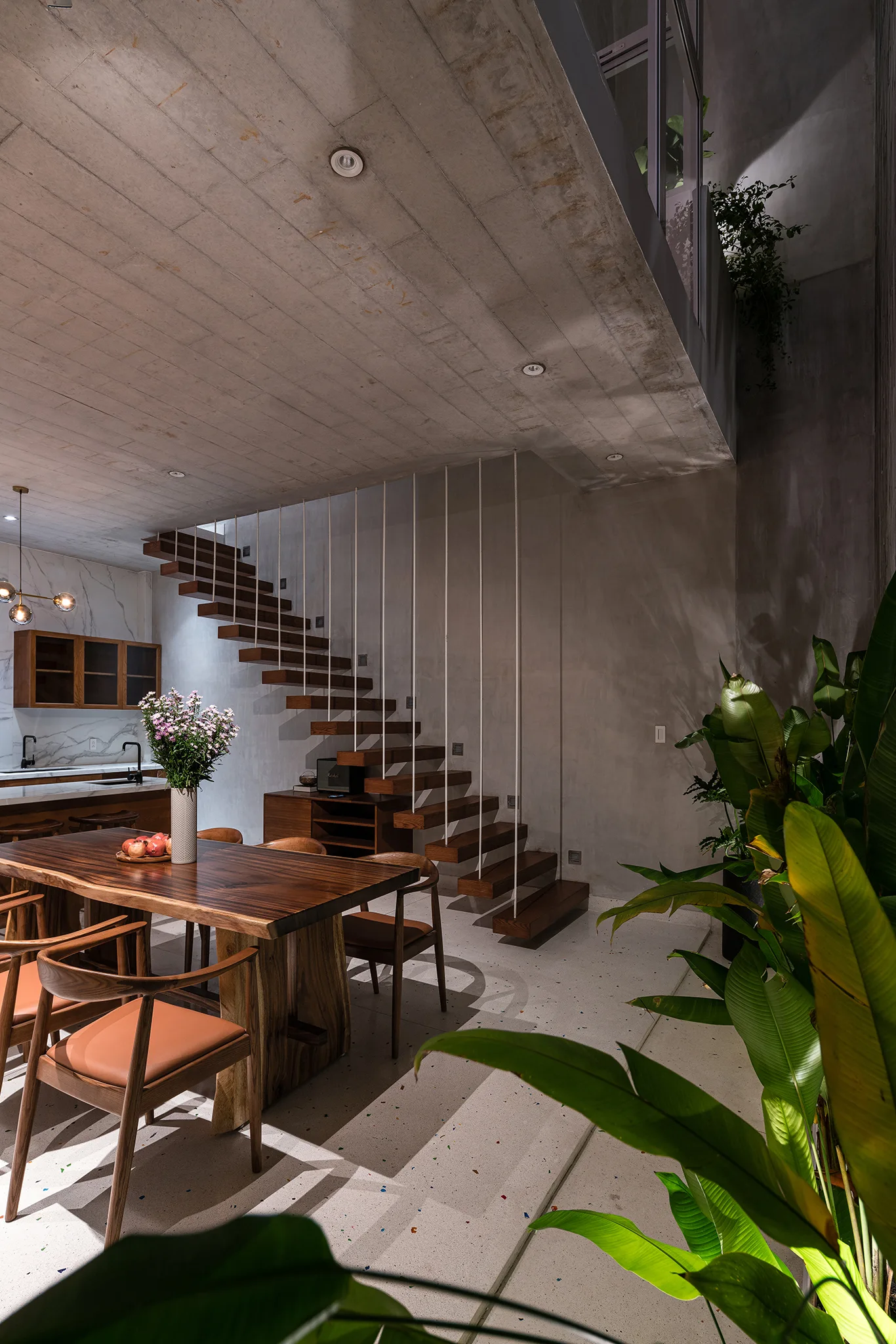 A modern dining room features a live-edge wood table and chairs next to an open-riser wooden staircase with vertical white support rods.