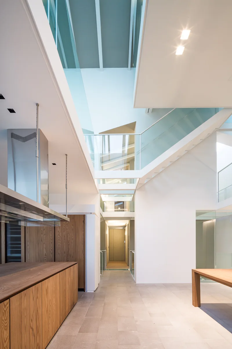 A modern multi-level interior featuring a floating staircase with glass railings, white walls, and warm wood cabinets.