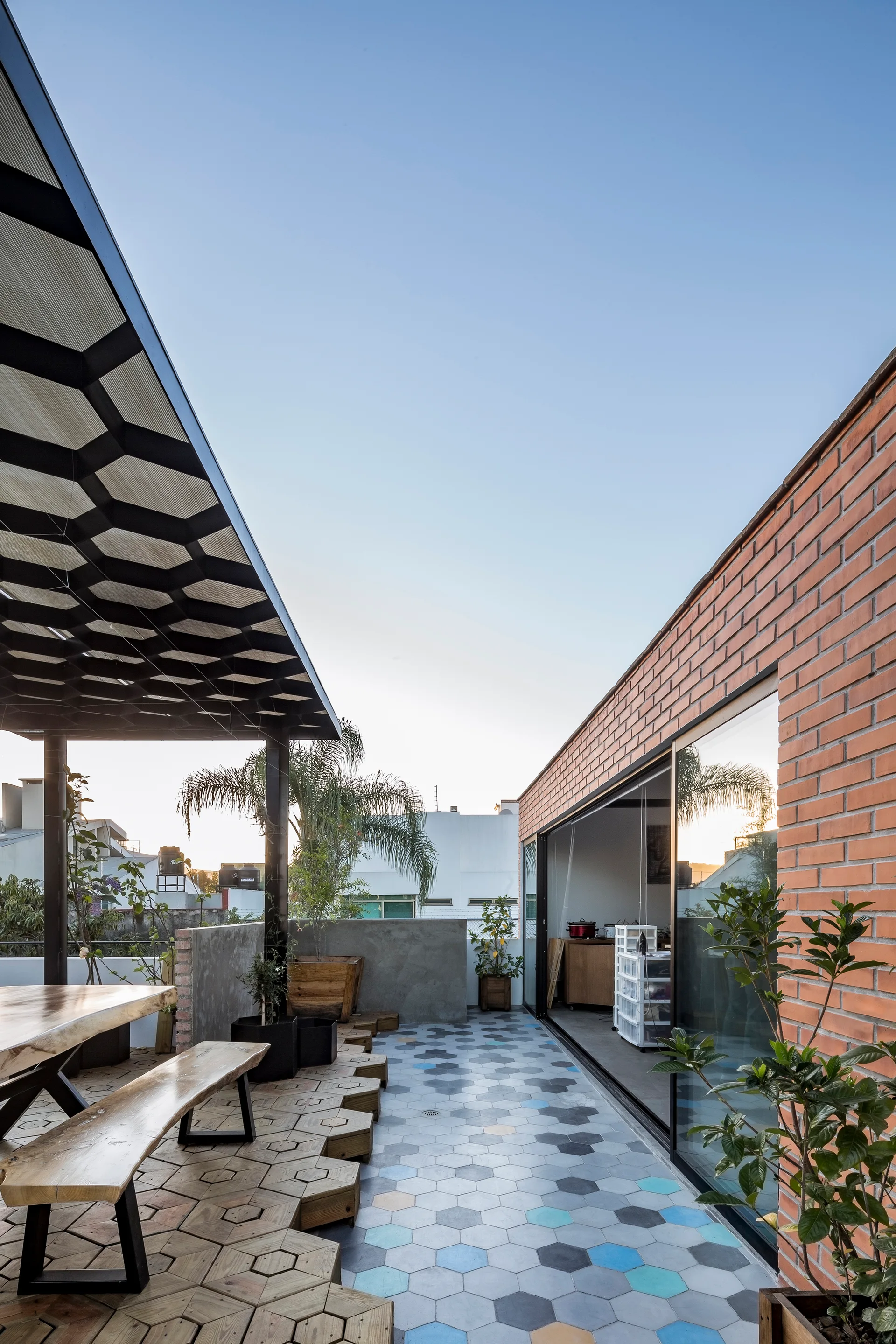 An outdoor rooftop patio featuring hexagonal wood decking, colorful hexagonal tiles, a matching dining set, and an exposed brick wall.