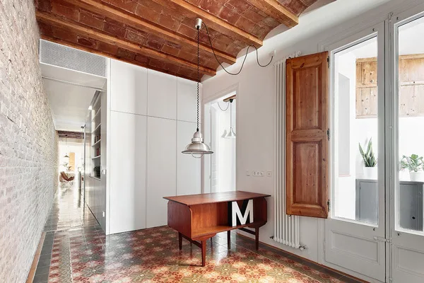 A bright hallway features a vaulted brick ceiling, ornate patterned floor tiles, and a mid-century modern wooden desk.