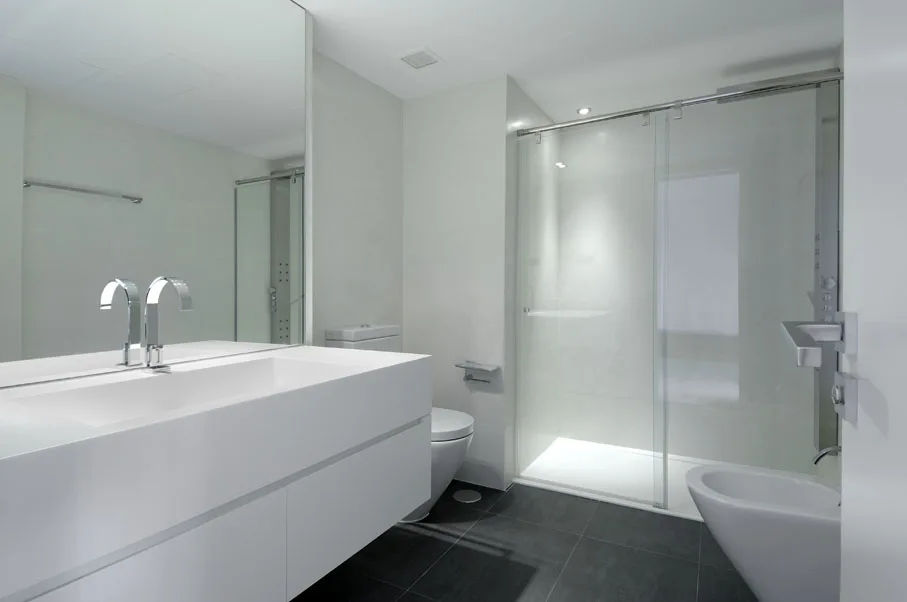 A modern white bathroom features a floating vanity with a chrome faucet, a large frameless mirror, and a glass-enclosed shower on dark gray tile flooring.