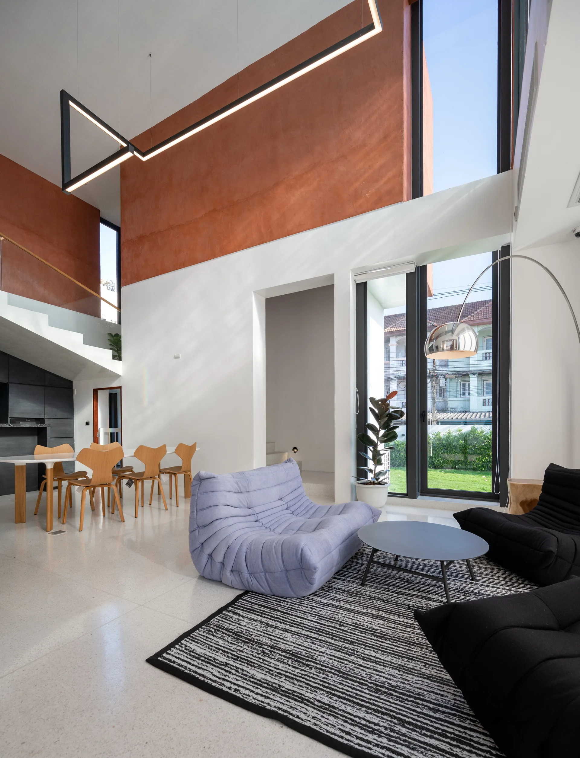 A double-height living room featuring a purple low-profile sofa, black armchairs, and a prominent terracotta accent on the upper wall.