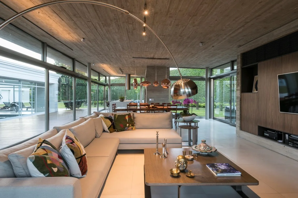An open-concept living room features a cream sectional sofa, a low wood coffee table, an arched floor lamp, and a textured concrete ceiling.