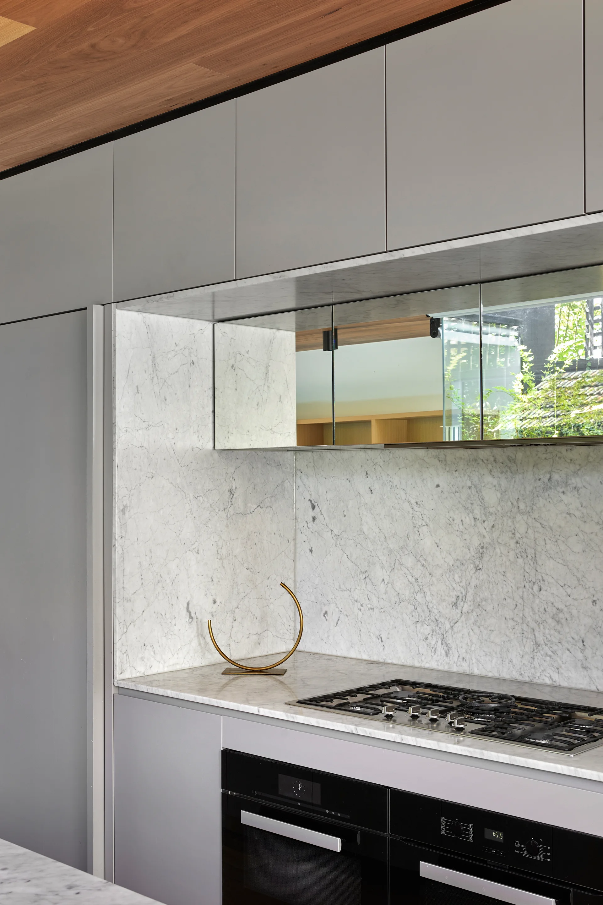 Matte grey kitchen cabinets surround a veined white marble backsplash and countertop with integrated black ovens.